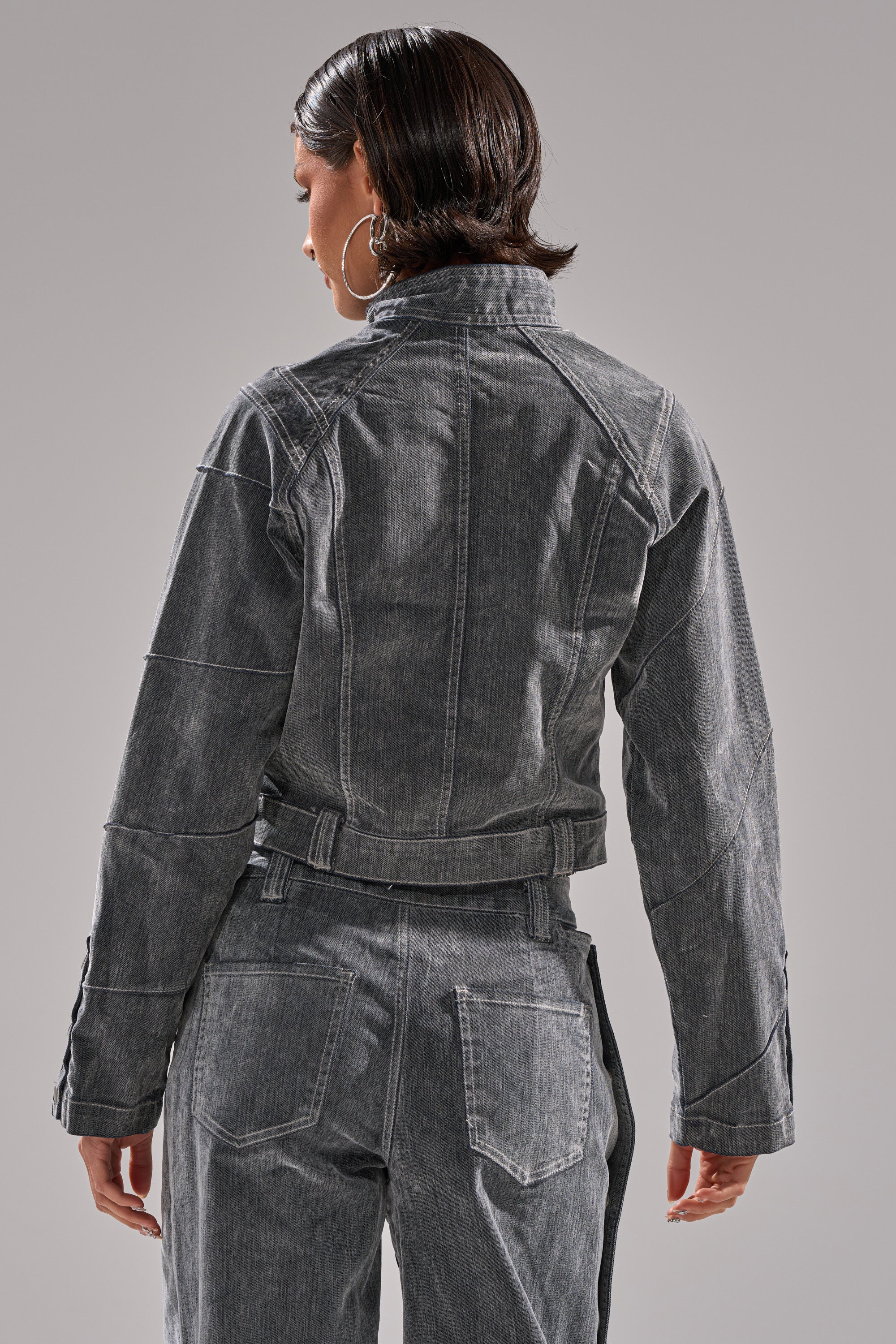 A person with short dark hair, large hoop earrings, and the CATCHING EYES VELVET DENIM BLOUSE paired with gray denim pants stands with their back to the camera against a neutral background.