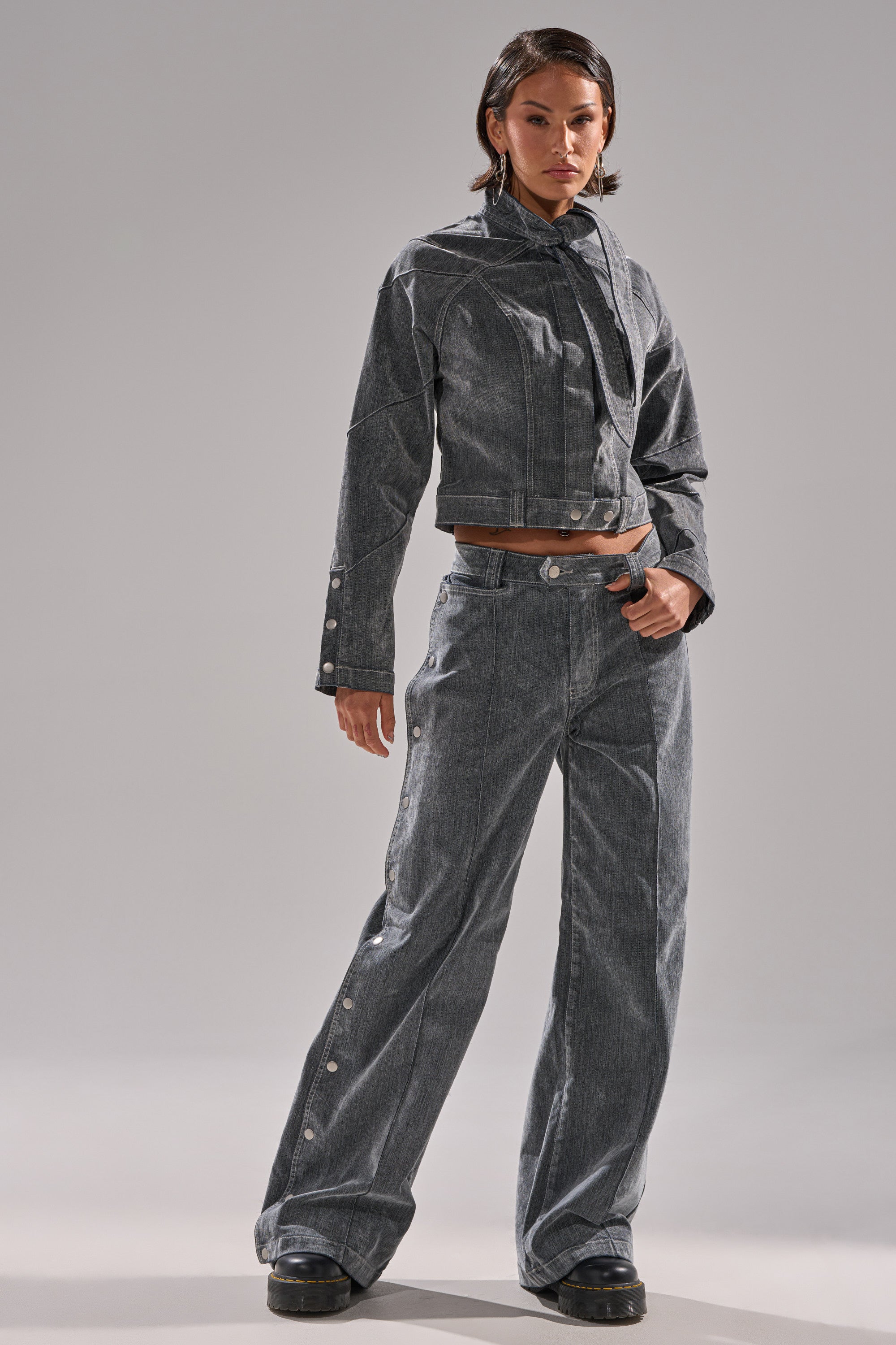 A woman with short dark hair poses confidently against a light background in the CATCHING EYES VELVET DENIM BLOUSE and matching gray wide-leg snap-button pants, paired with chunky black shoes.