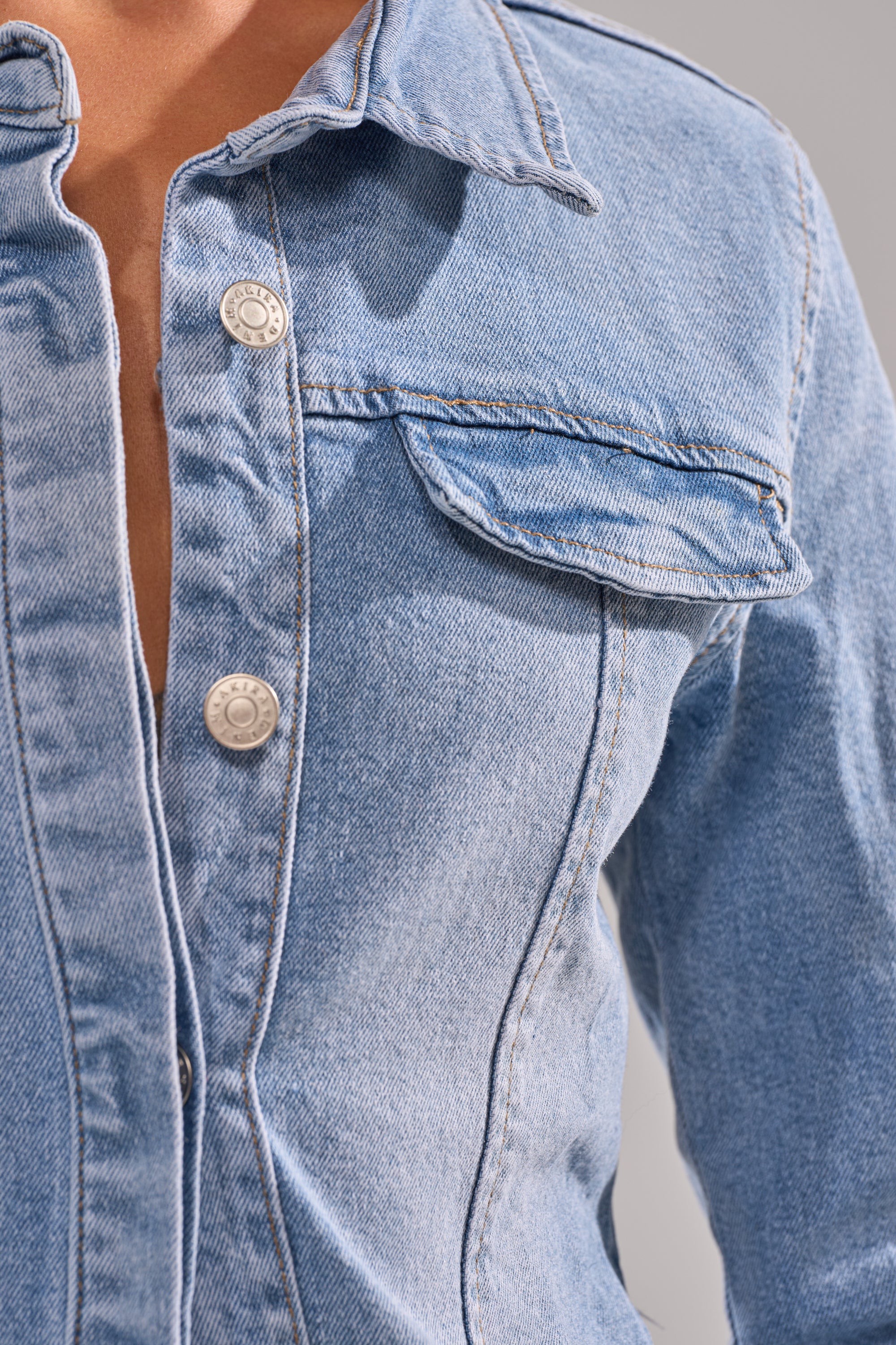 Close-up of a person wearing the ROCK MY WORLD DENIM BUTTON DOWN in light blue with metal buttons, a chest pocket, and part of the collar and upper torso visible.