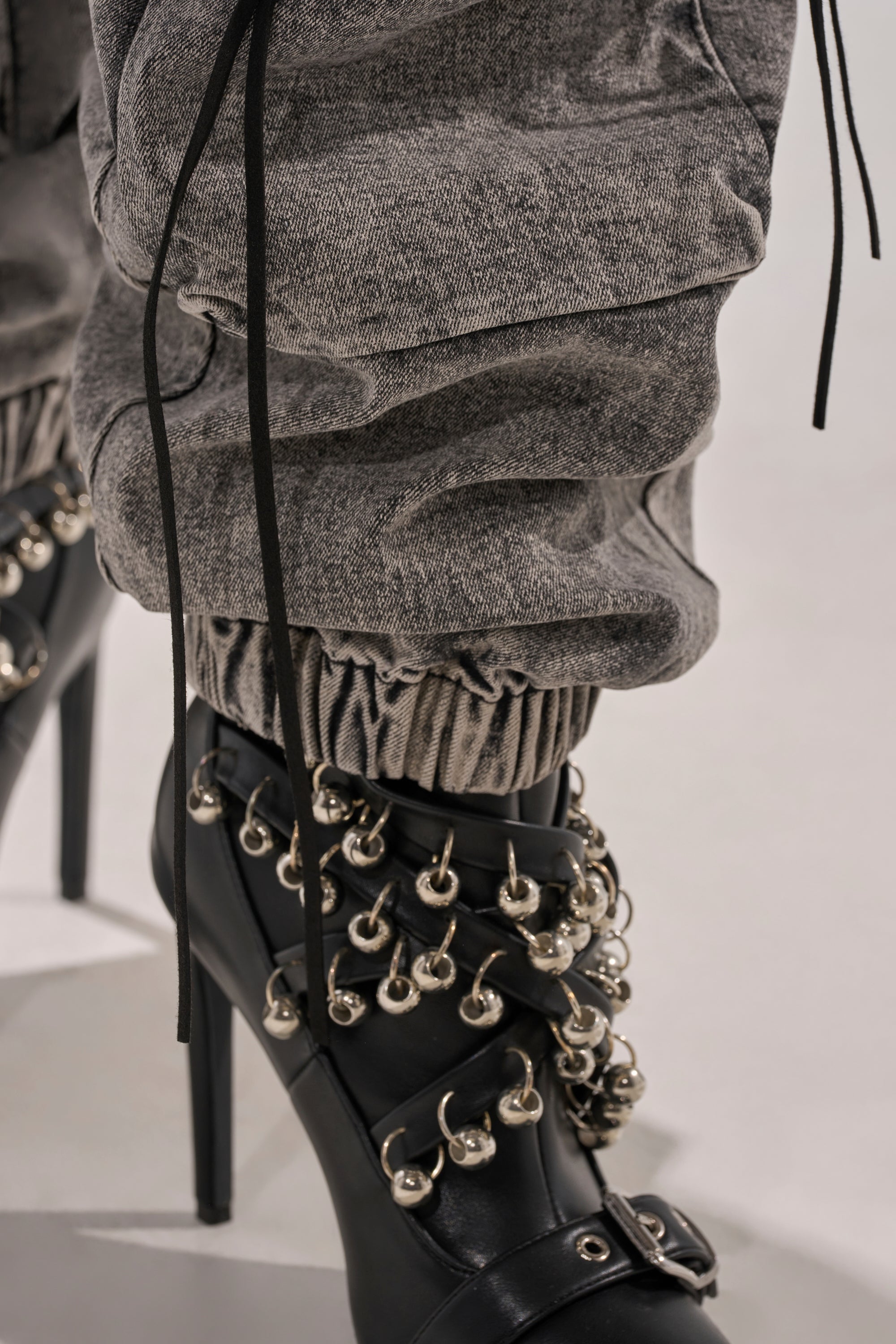 Close-up of the CARGO FOR DAYS DENIM JOGGER in gray, ruched and tucked into black high-heeled boots with metallic rings and studs, delivering a bold, edgy streetwear vibe.