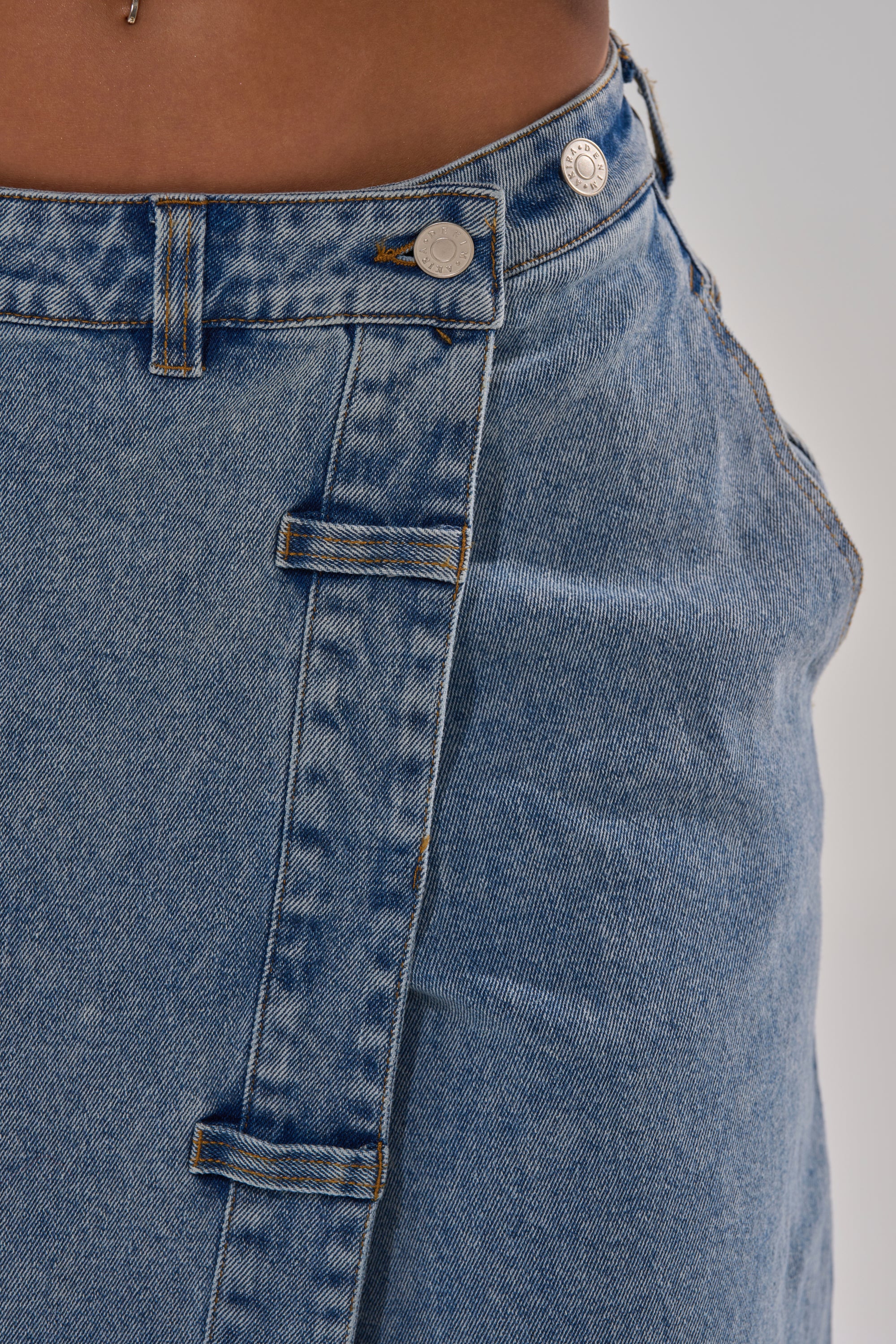 Close-up of the waistband and upper section of the COVERED UP RELAXED DENIM PANT, featuring decorative belt loops and metal buttons inspired by classic high-rise denim styles, worn by a person with brown skin.