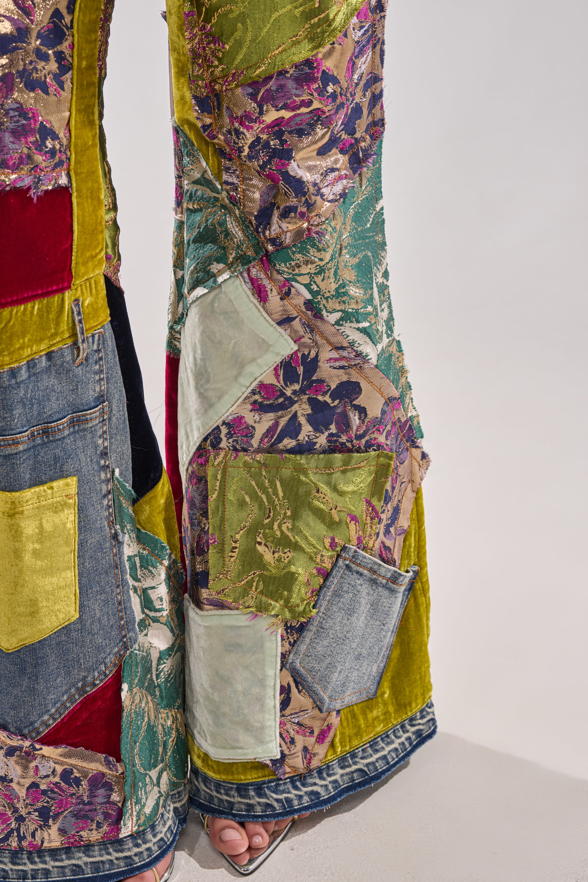 A close-up highlights the MIXED EMOTIONS BROCADE PATCHWORK FLARE DENIM, featuring high-rise street-style patchwork with colorful velvet, floral prints, and denim squares, paired with open-toe sandals.