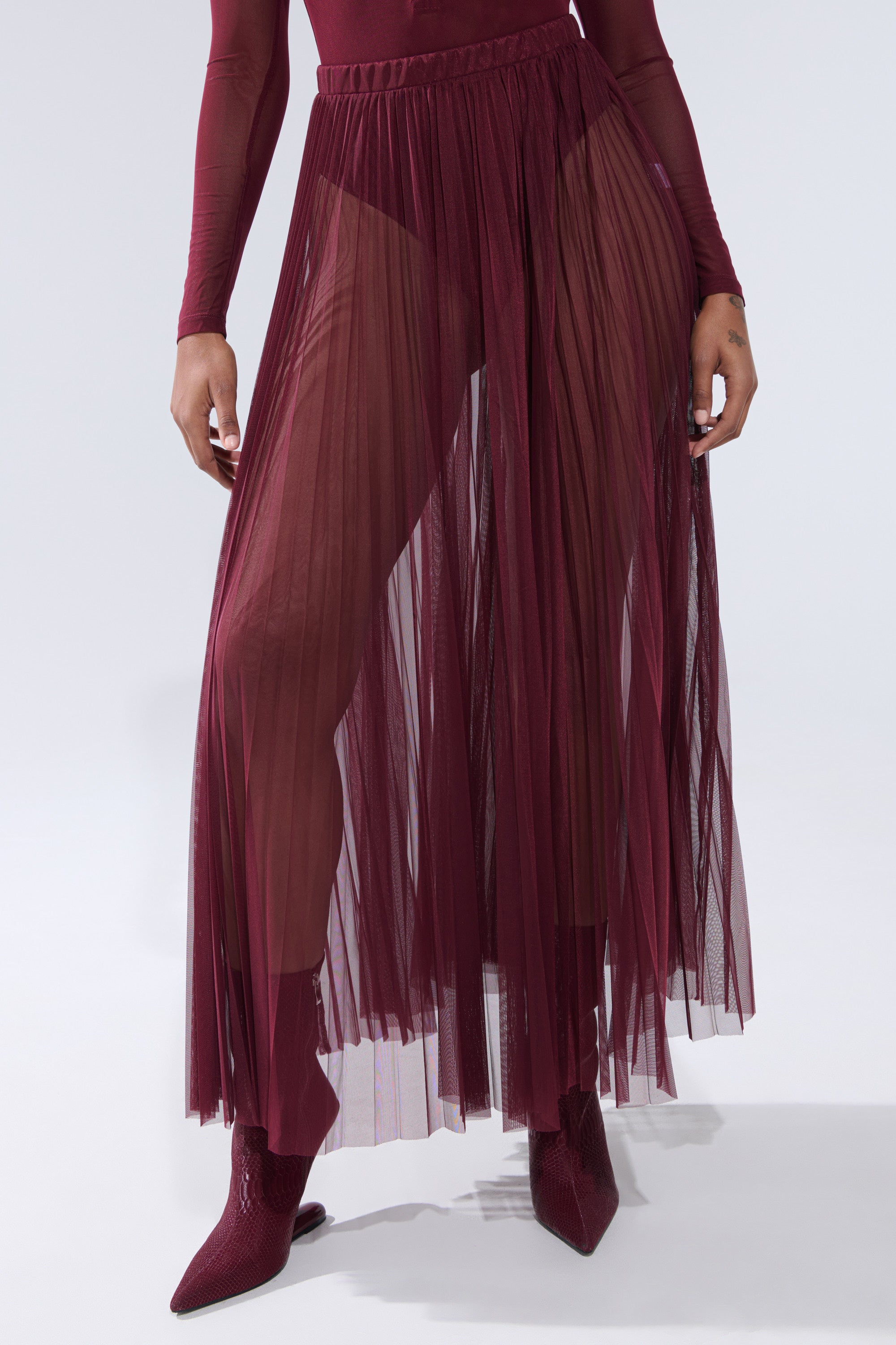 A person styles the ON FIRE MESH MAXI SKIRT in burgundy over high-waisted briefs, with pointed burgundy boots and a long-sleeved top. 0
