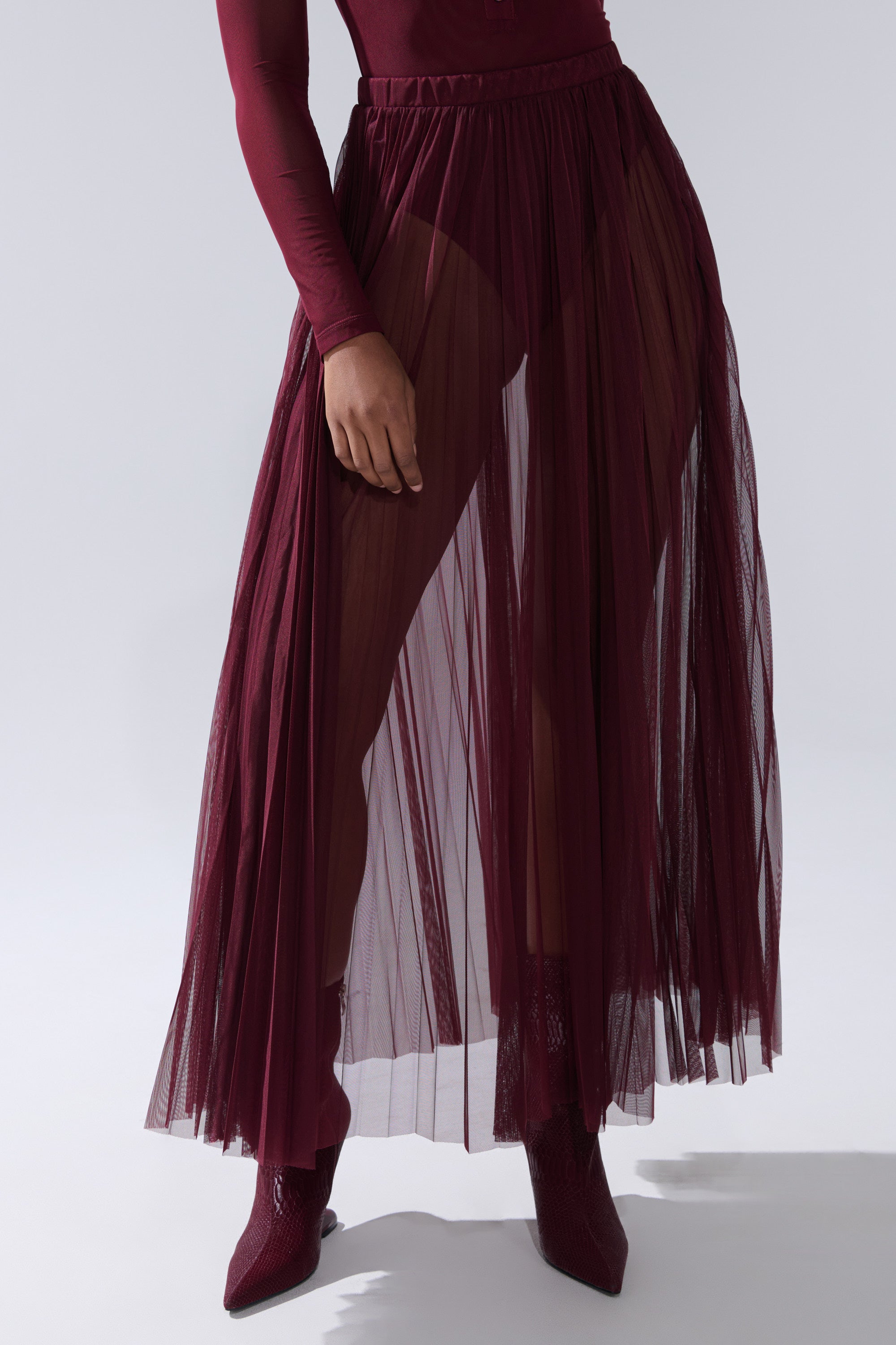 Model wearing the ON FIRE MESH MAXI SKIRT in burgundy, paired with a matching long-sleeve top and pointed-toe boots, standing against a plain light backdrop. Face is not visible. 7