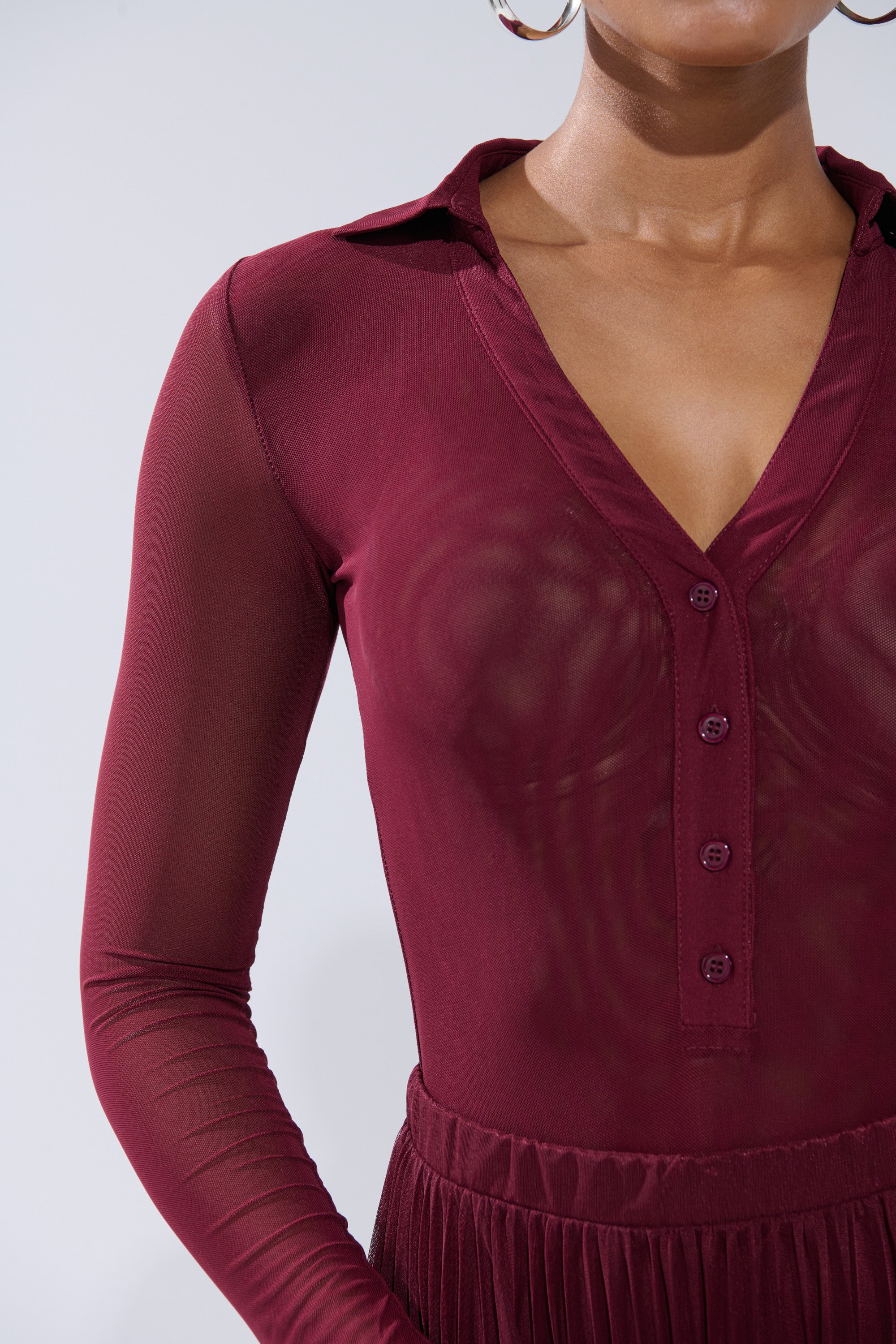 A person wears the ON FIRE MESH BODYSUIT—sheer, curve-hugging, long-sleeve, deep burgundy with a collared neckline and four buttons—paired with a matching waistband. Large hoop earrings are visible; face is partially out of frame. 9