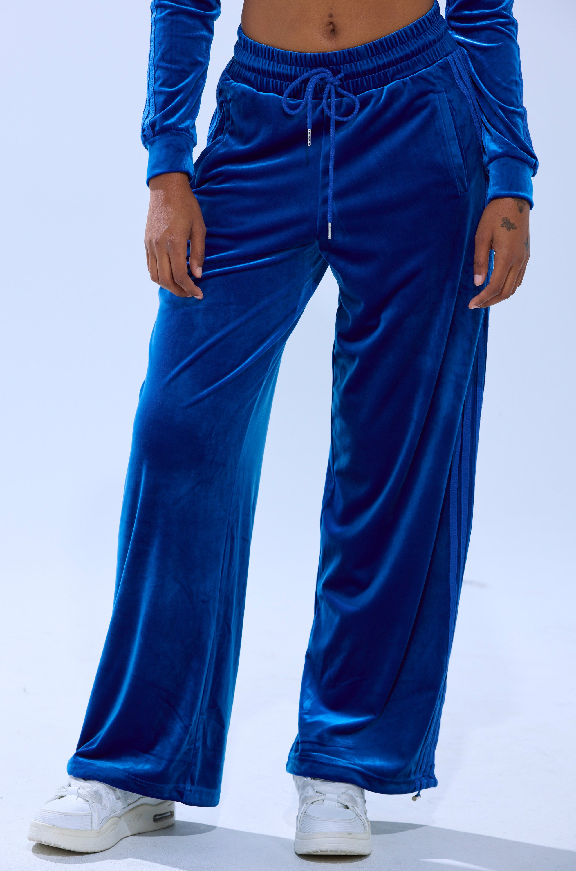 Wearing ELECTRIC BLUES WIDE LEG JOGGER in royal blue with a matching long-sleeve top and white sneakers, person stands against a plain light background; only the lower body is visible.