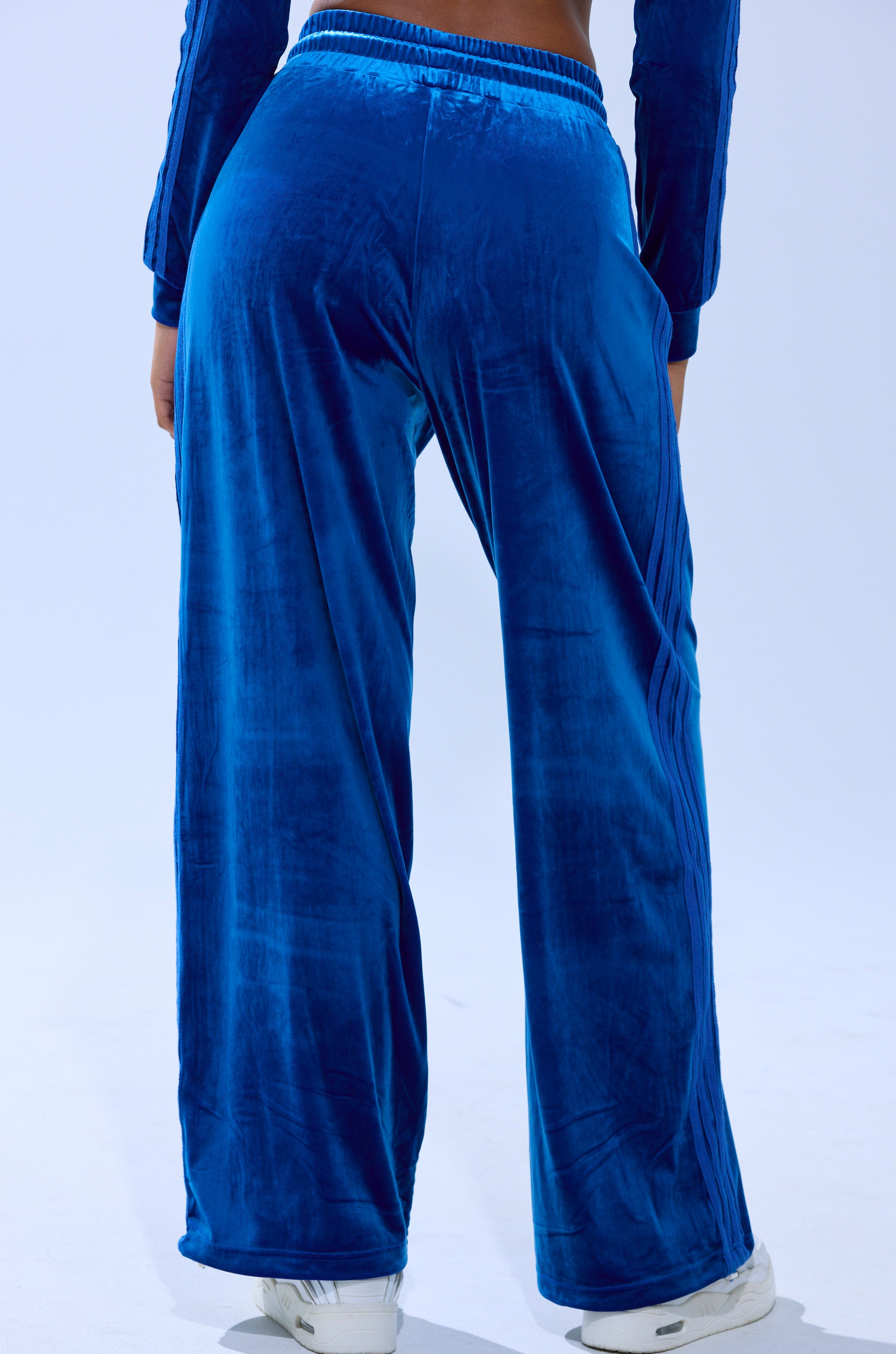 Person wearing ELECTRIC BLUES WIDE LEG JOGGER pants and matching top, photographed from behind on a light surface with white sneakers visible.
