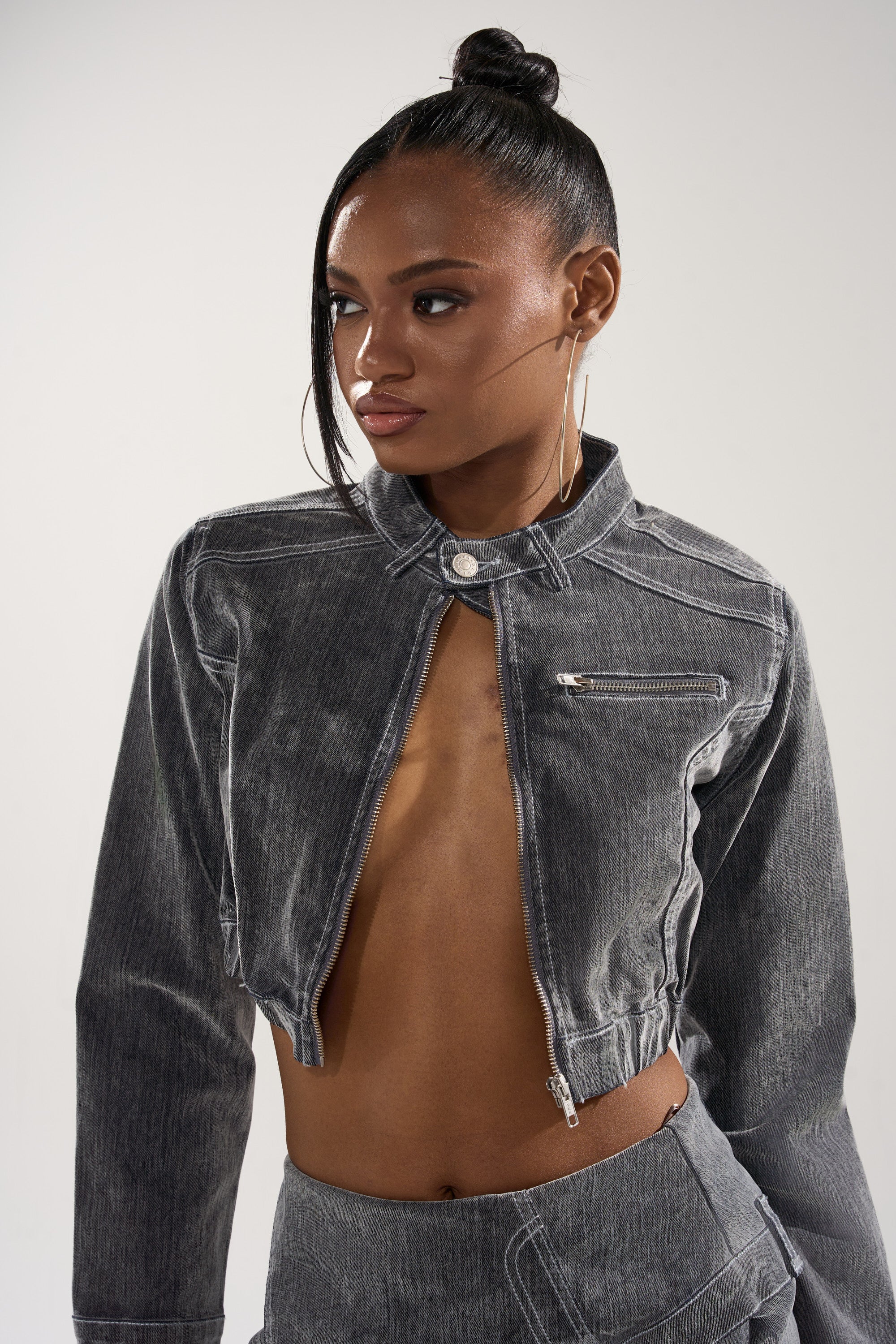A woman with hoop earrings and sleek hair models the ALL FOR LOVE VELVET DENIM MOTO jacket, featuring a cropped cut and front zipper pocket, against a plain light background.