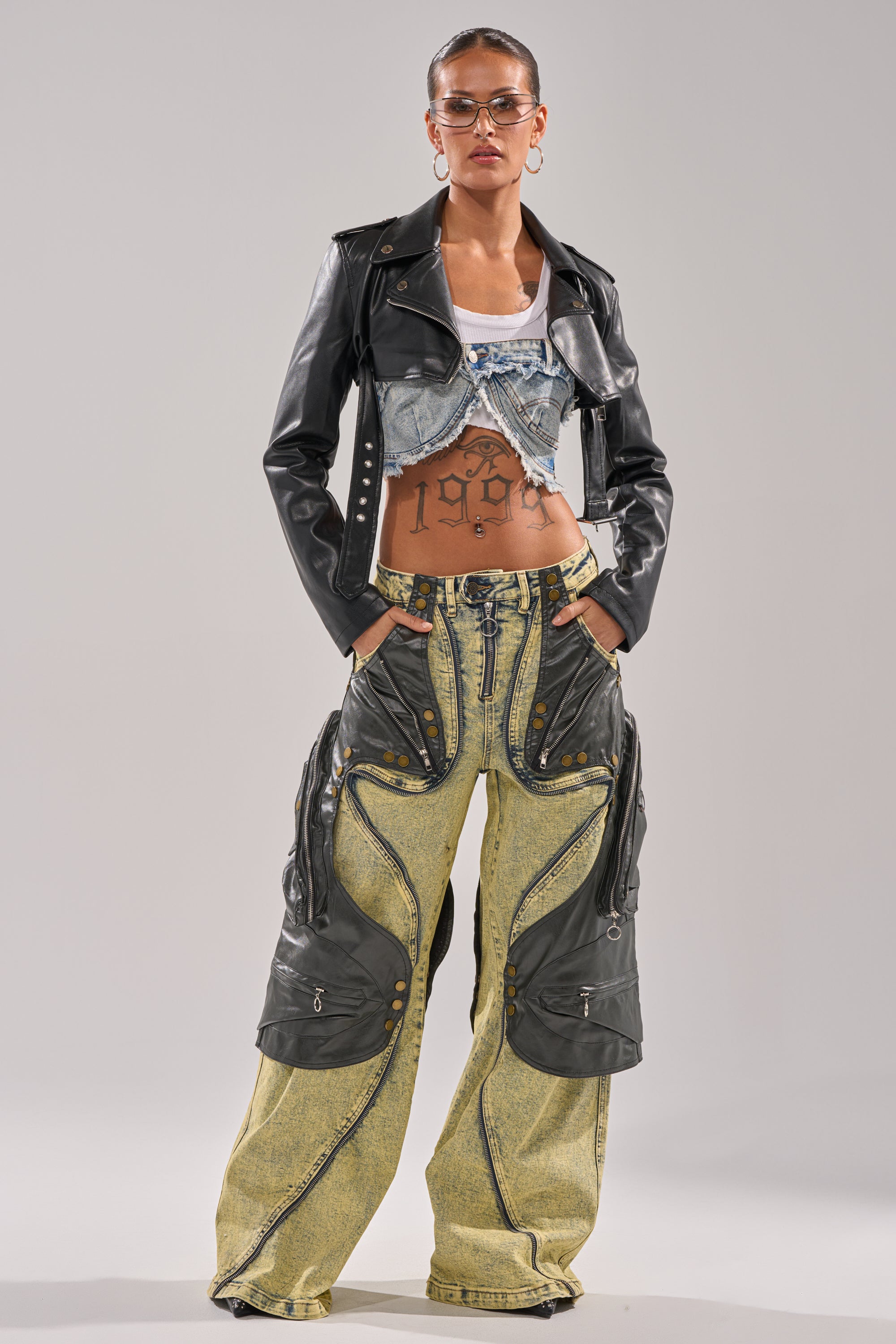 Wearing glasses and a cropped leather jacket over the CRAZY FOR YOU RELAXED DENIM top, this confident individual pairs yellow faux-leather paneled wide-leg pants with slicked-back hair and a "1996" tattoo on their torso. 9