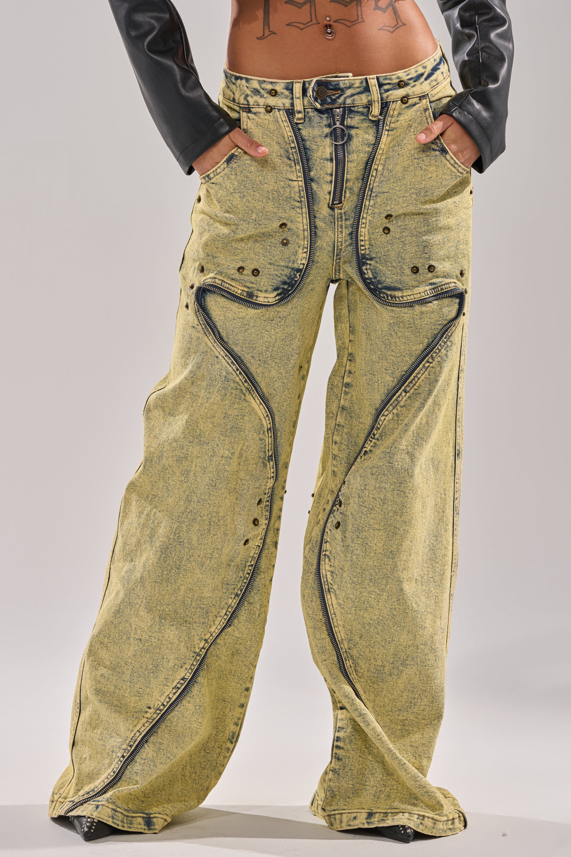 A person wearing the CRAZY FOR YOU RELAXED DENIM: wide-leg, high-waisted acid-wash yellow jeans with black detailing and curved seams; hands in pockets, paired with a cropped black leather jacket for a bold, relaxed denim look. 2
