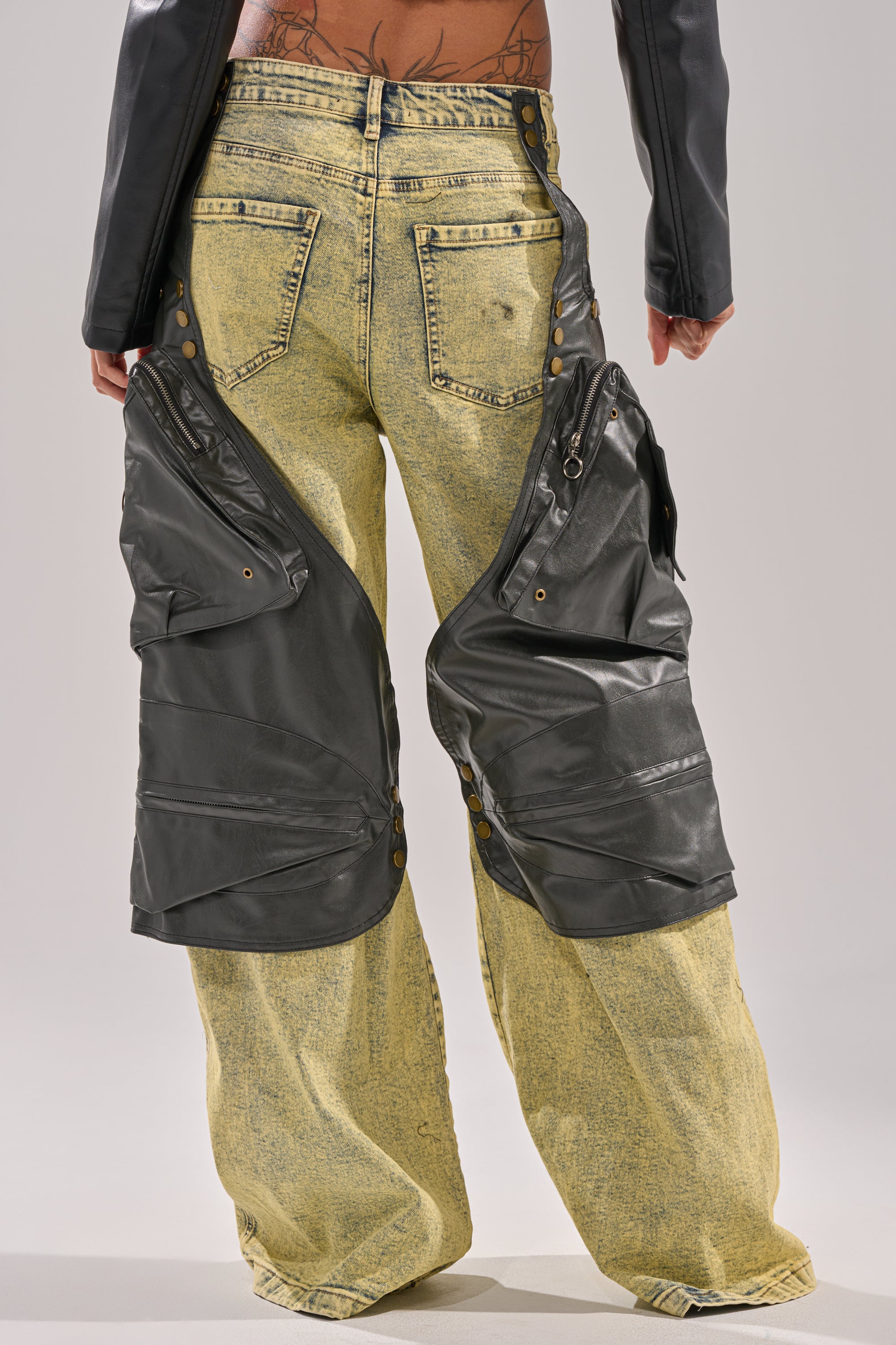 A person is seen from the back wearing CRAZY FOR YOU RELAXED DENIM—acid wash jeans with large black faux leather thigh panels. Their lower back tattoo is partially visible above the waistband. 7