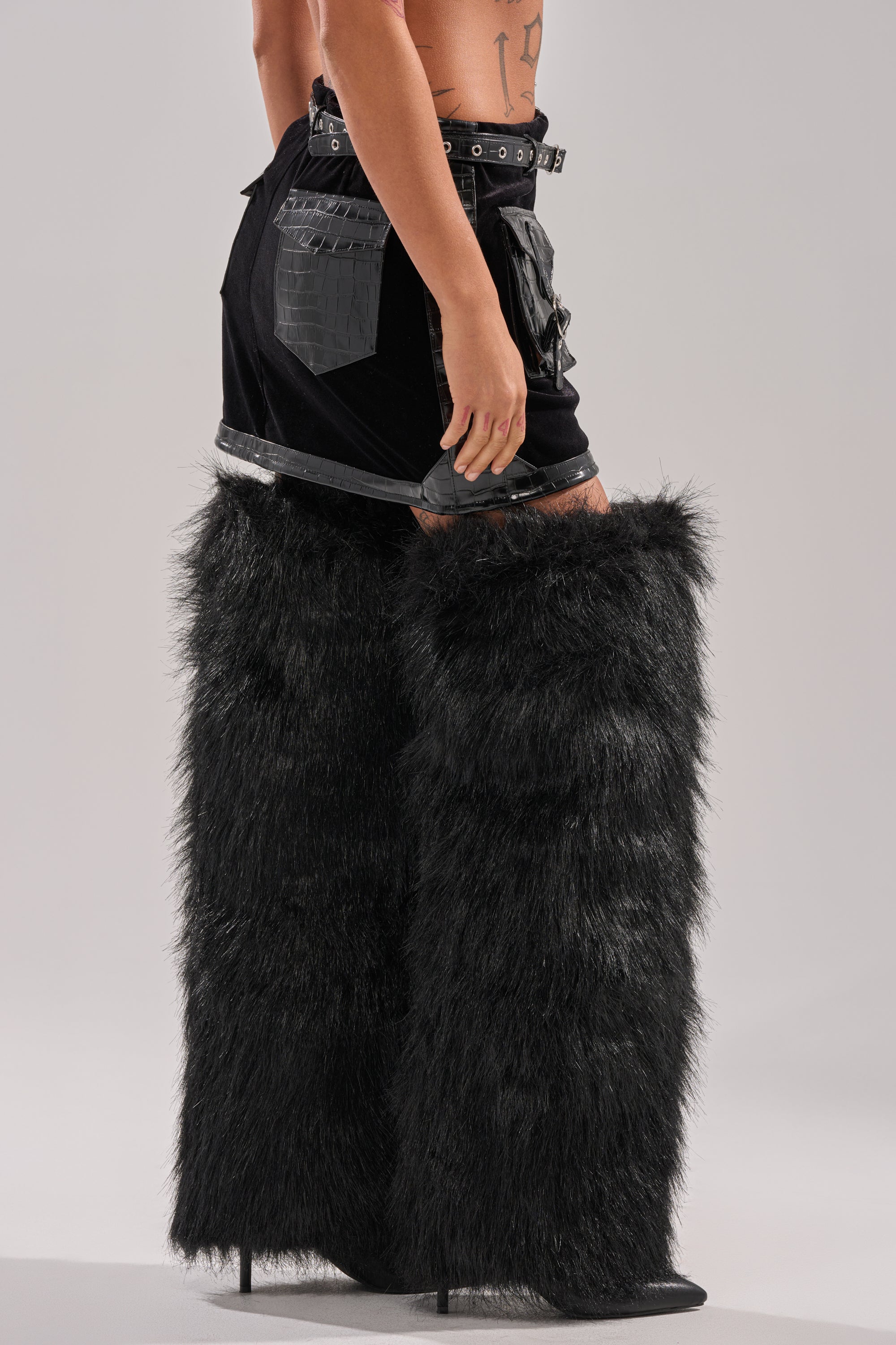 A person wearing the FEELING CRAZY MINI SKIRT and oversized black furry thigh-high boots stands against a plain light gray background.