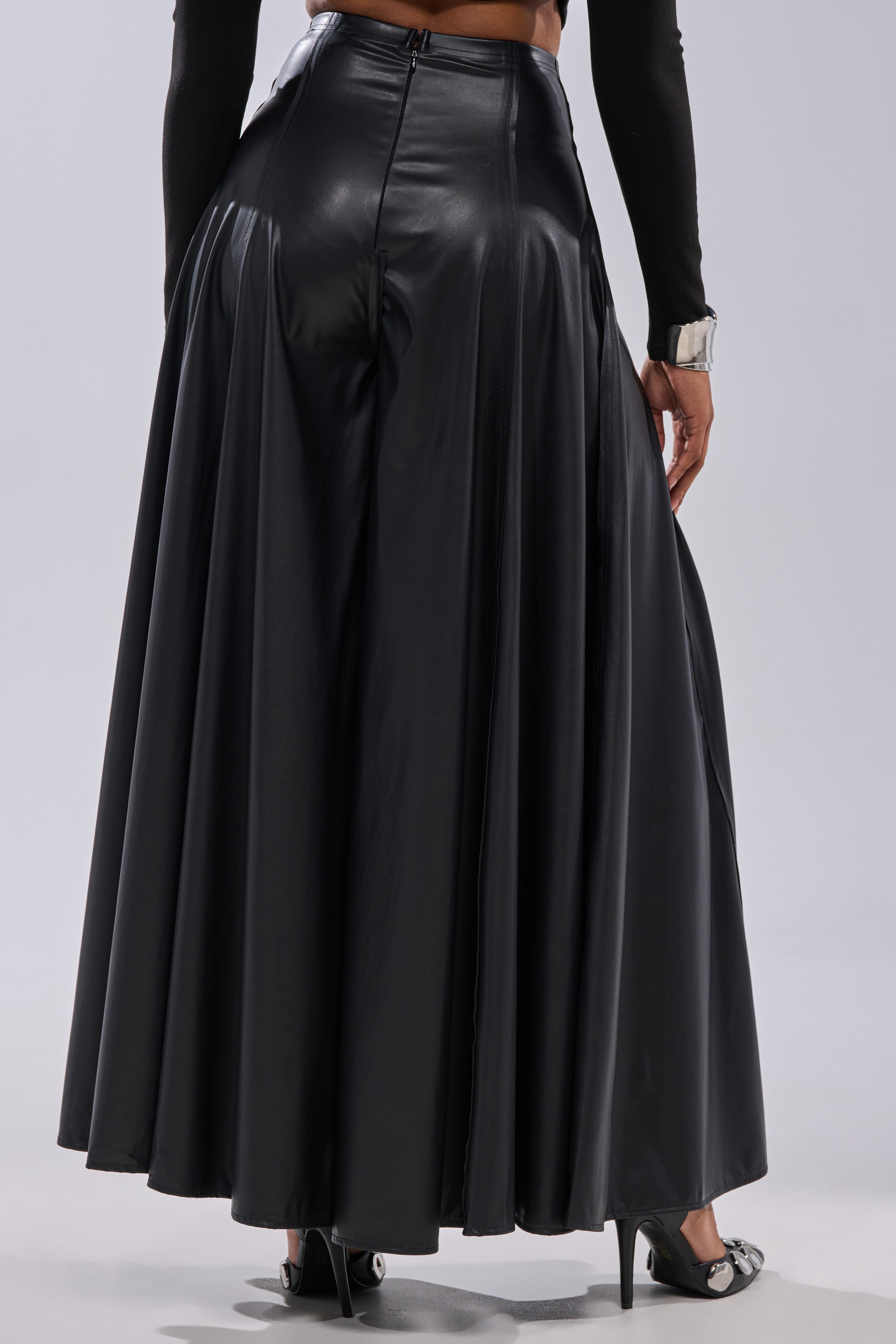 A person wears the GALAXY FAUX LEATHER TROUSER with a high-rise waist and ankle-length cut, styled from the back with black heels and a fitted black top for an elegant look. 4