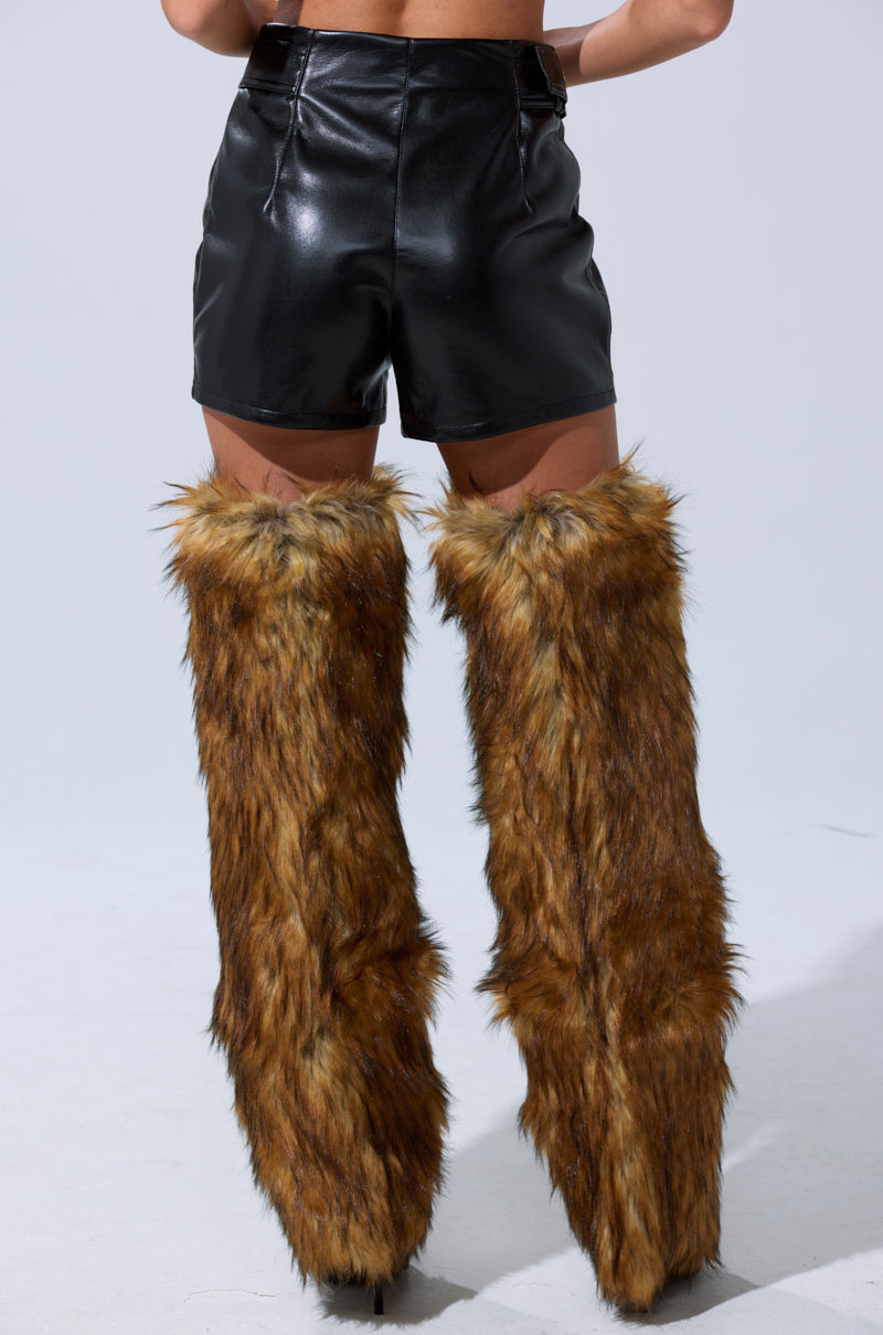 Someone is seen from the back against a plain light background wearing the BUILD ME UP FAUX LEATHER SHORT with buckle detail and tall brown faux fur leg warmers. 6