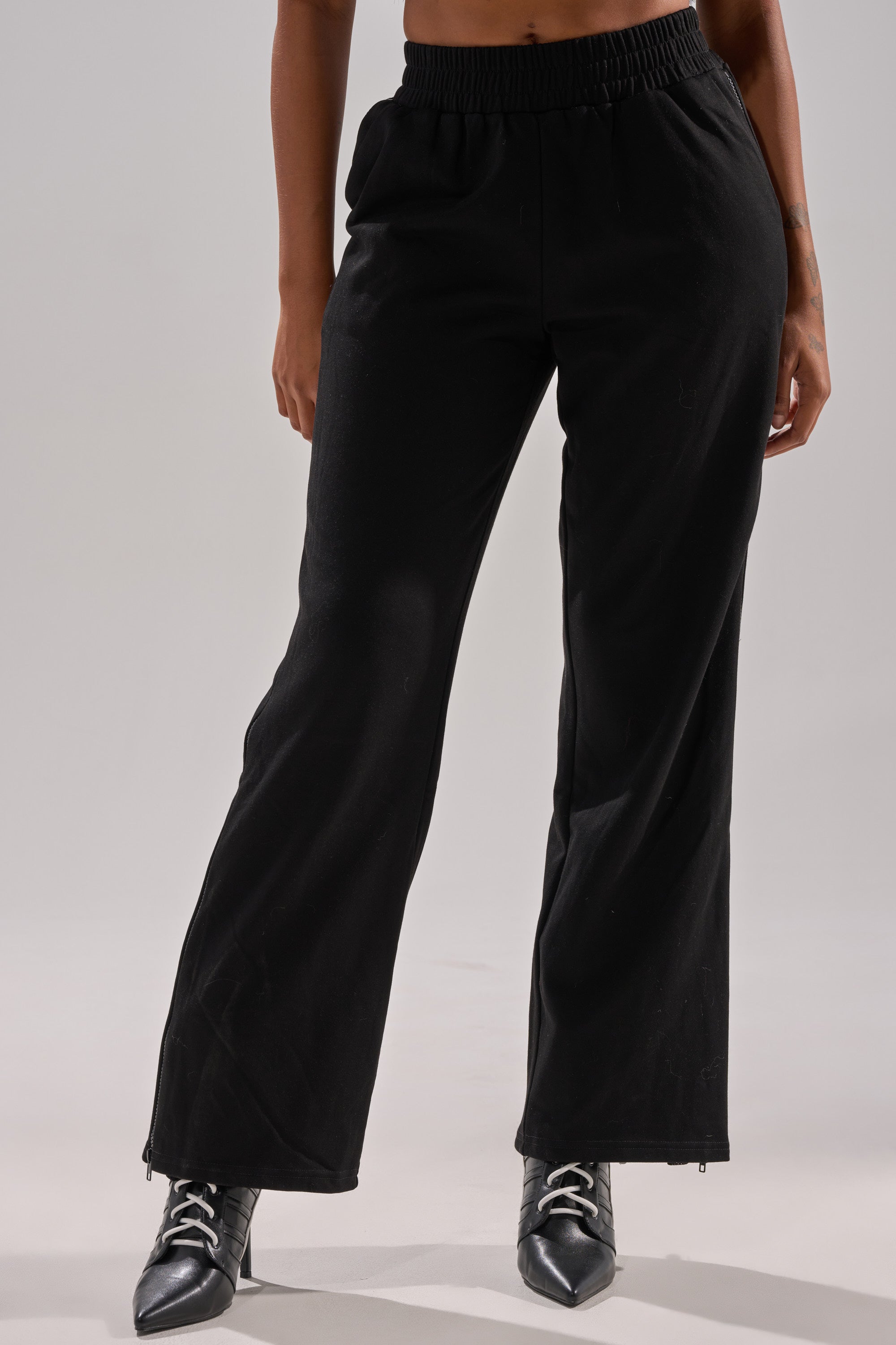 Someone wearing the OPEN UP WIDE LEG JOGGER WITH RHINESTONE, featuring an elastic waistband, paired with black pointed-toe lace-up boots, stands against a plain light background. 2