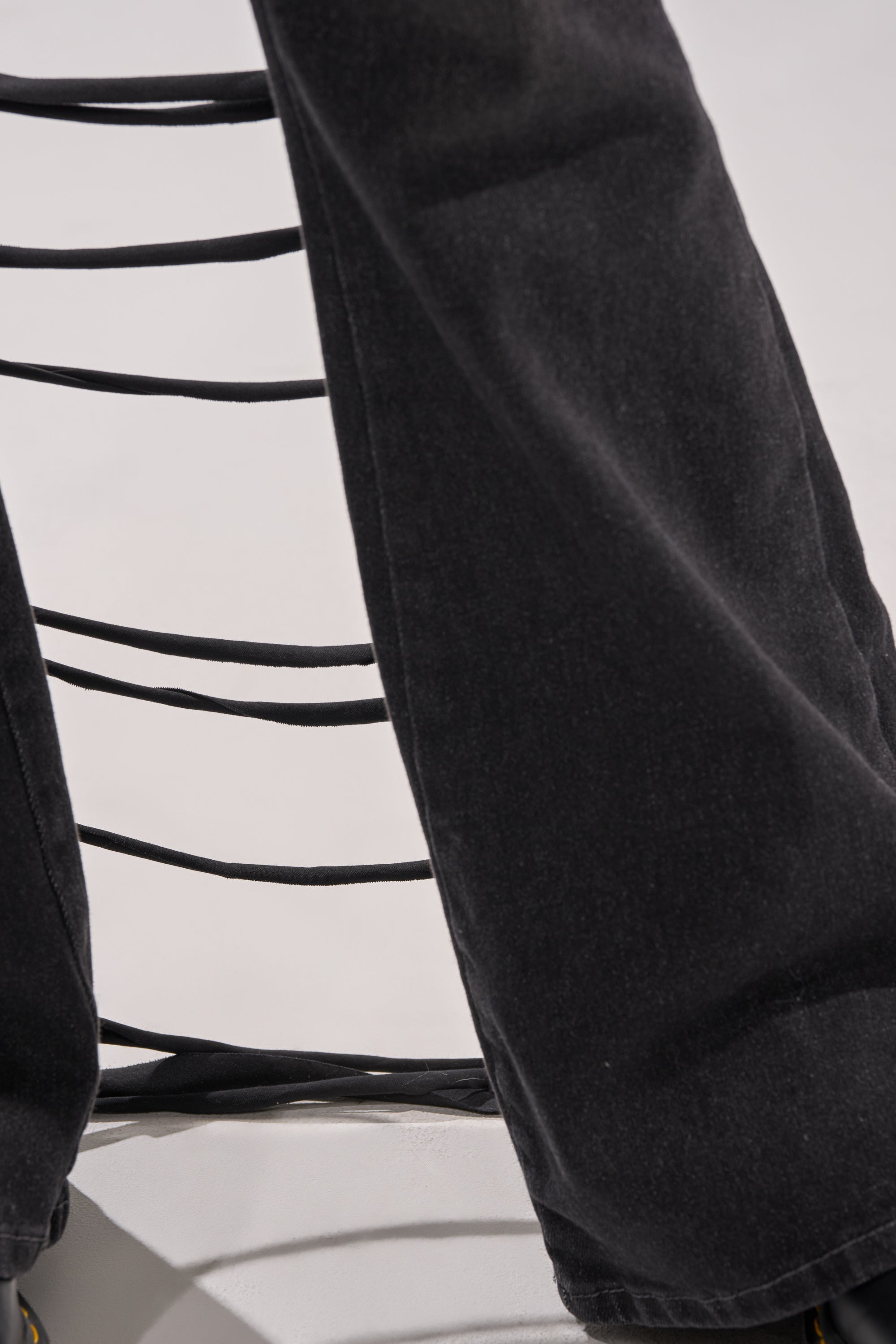 Close-up of TRY ME FLARE DENIM high-rise, wide-leg jeans draped over a chair's slatted black backrest, set against a plain light background. 6