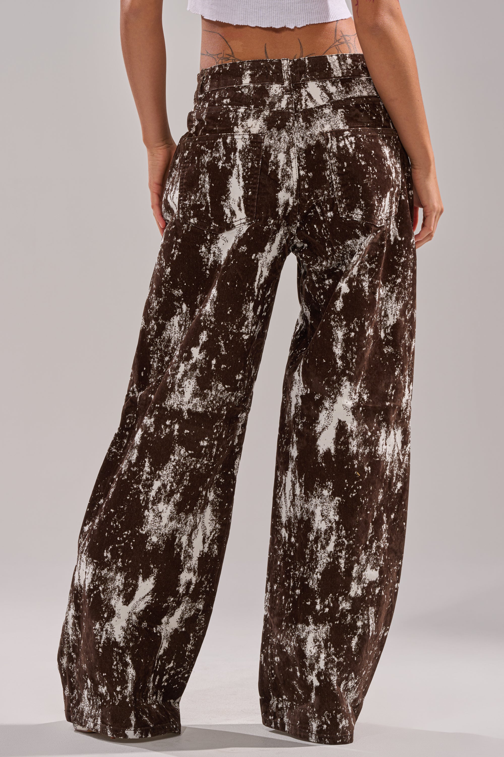 A person models the CRAZY IN LOVE TROUSER—loose, high-waisted suede-like denim with a white tie-dye pattern—paired with a white crop top, standing out against a plain neutral background. 4