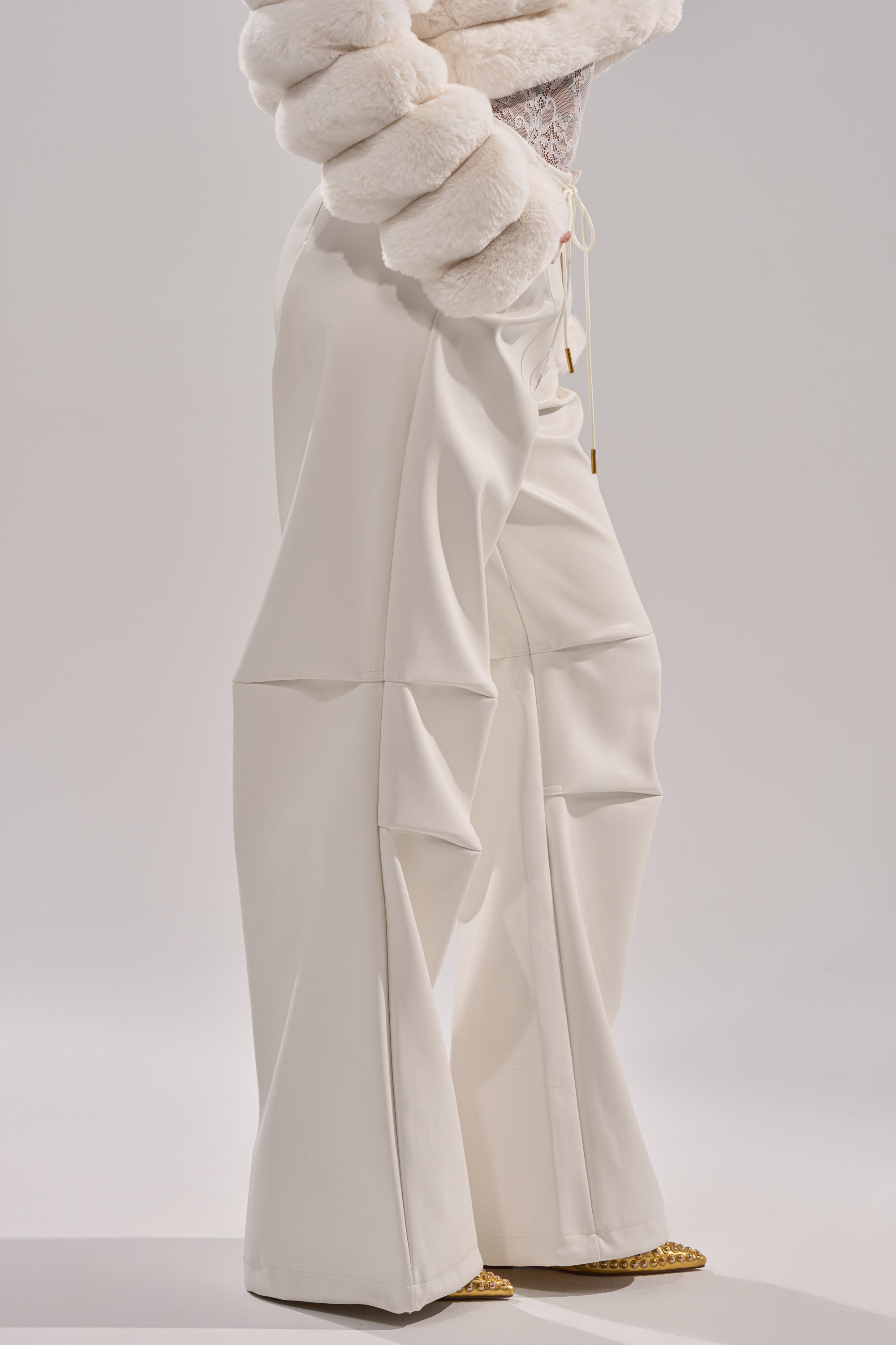 Wearing GET WITH IT FAUX LEATHER TROUSER IN WHITE, featuring wide legs and folded details, paired with a textured, fur-like white jacket; only the lower half of the body is shown against a plain background. 4