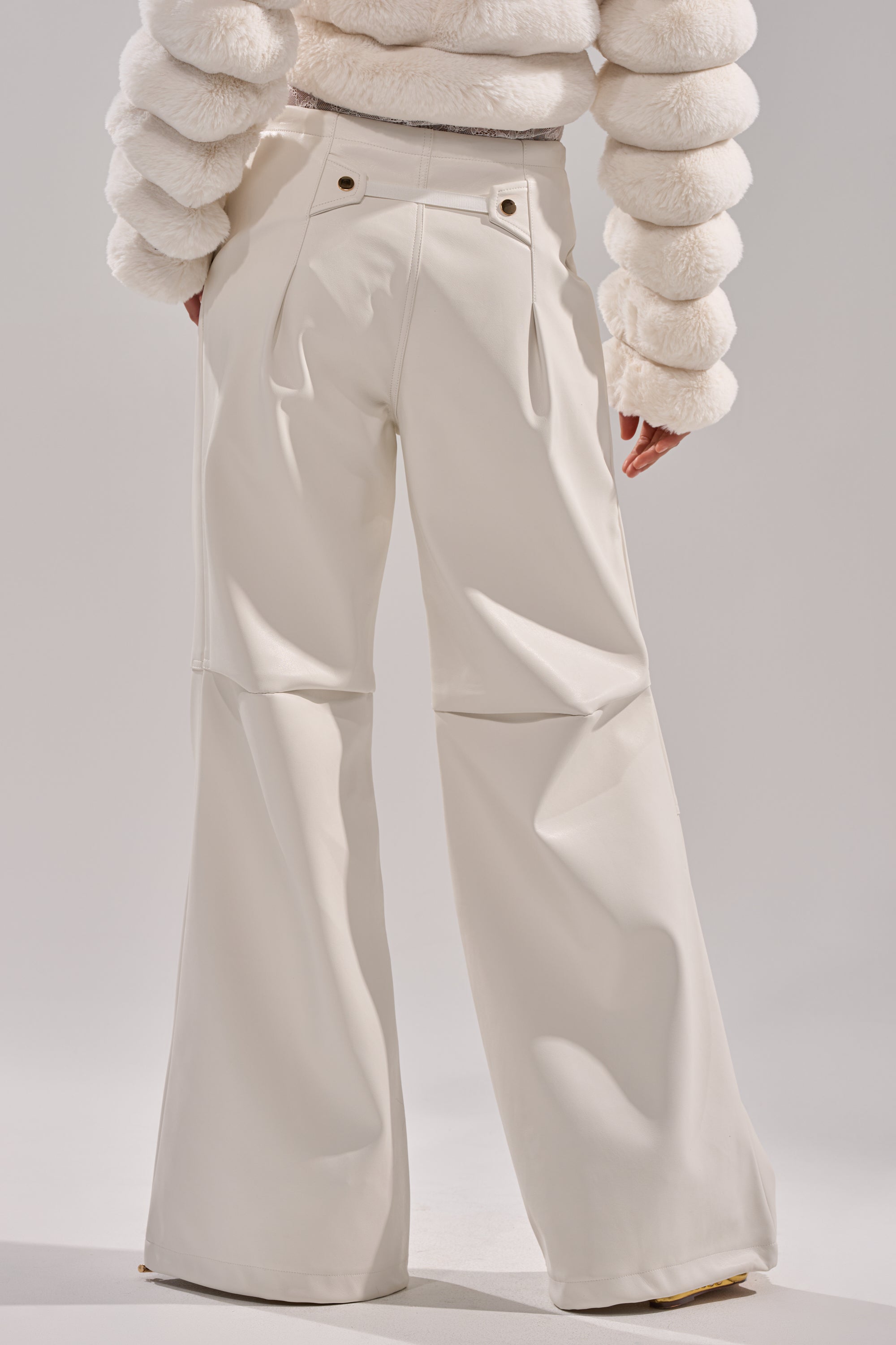 A person wearing GET WITH IT FAUX LEATHER TROUSER IN WHITE stands facing away against a plain background, paired with a textured, puffy-sleeved white top. 5