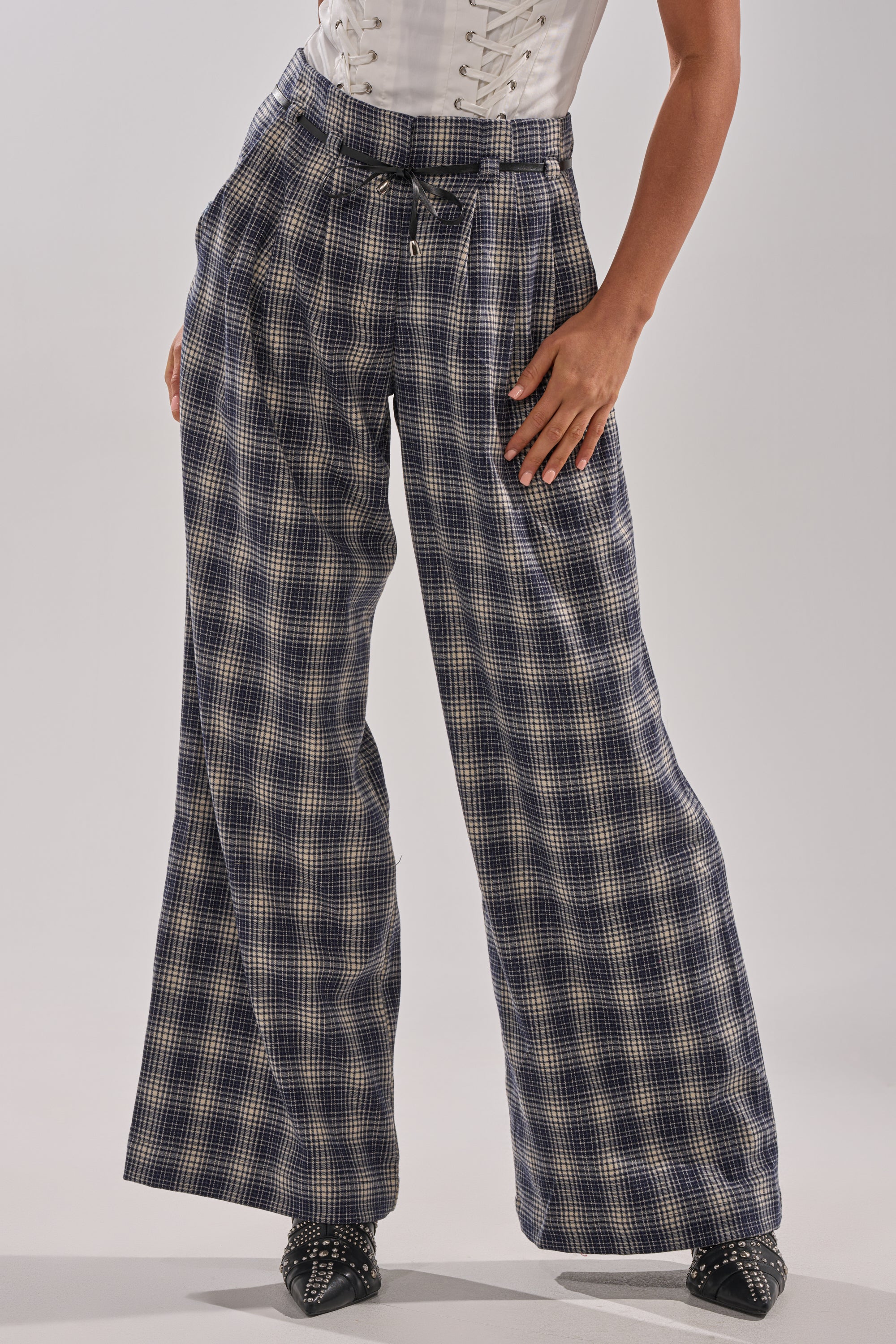 Wearing the JANE PLAID TROUSER in blue and white, styled with a white lace-up top and black studded pointed shoes. The person's head is not visible. 2