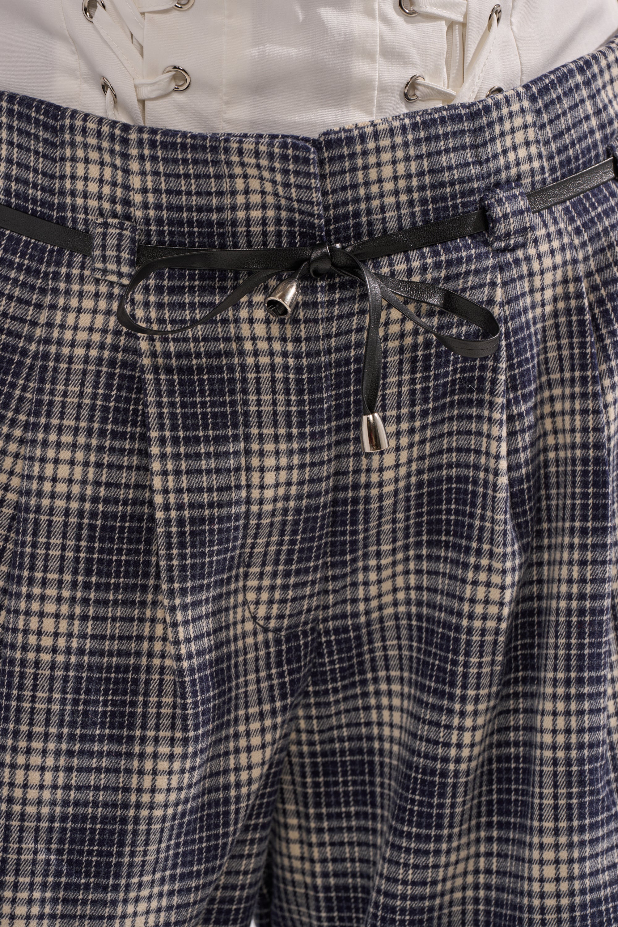 Close-up of the JANE PLAID TROUSER in blue and white plaid with a black drawstring belt at the waist, paired with a white top featuring decorative lacing above the waistband. 7