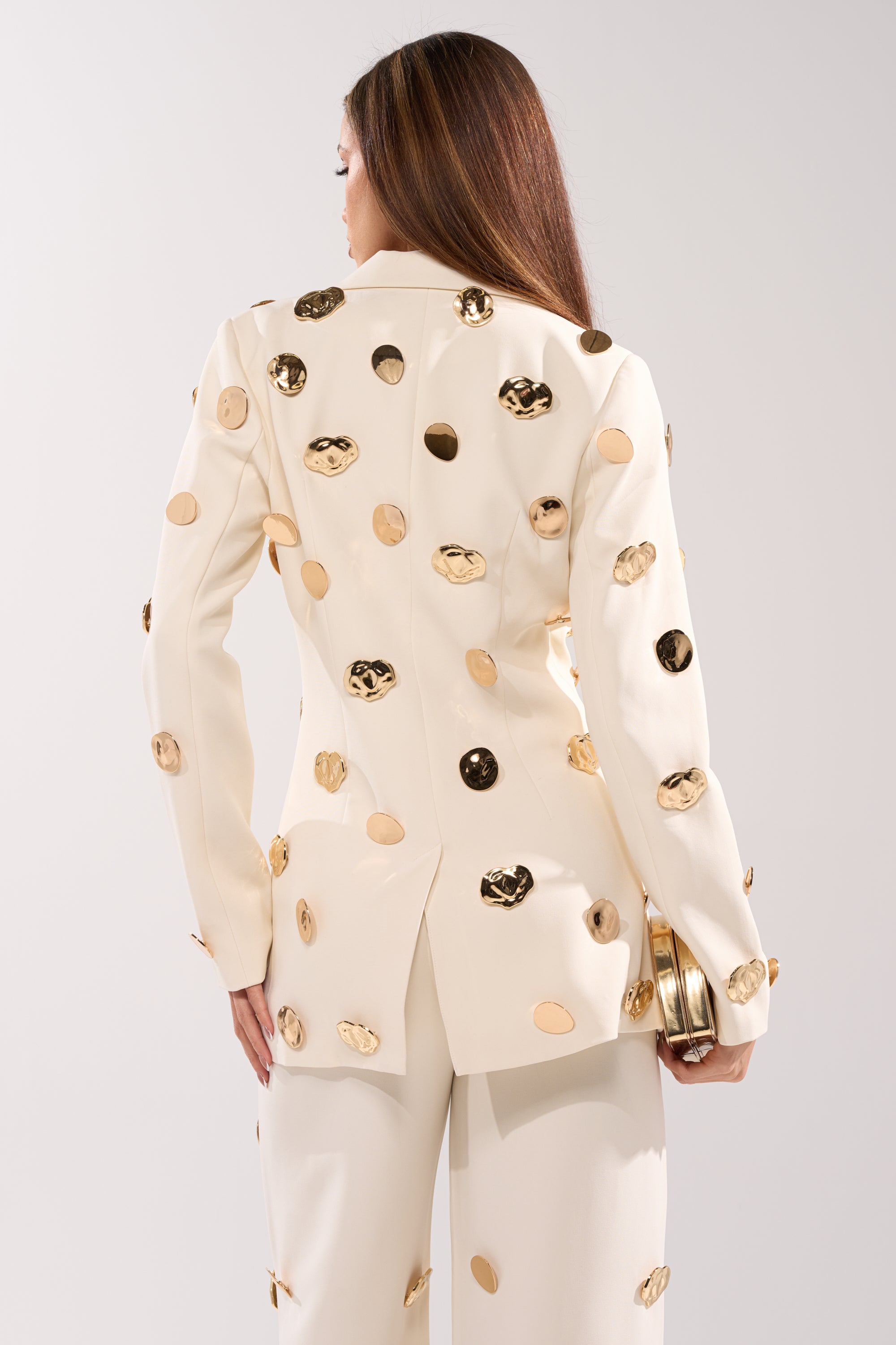 A woman with long brown hair, seen from behind, wears the SARASOTA EMBELLISHED BLAZER with matching pants and holds a small gold clutch in her left hand against a plain light background. 6