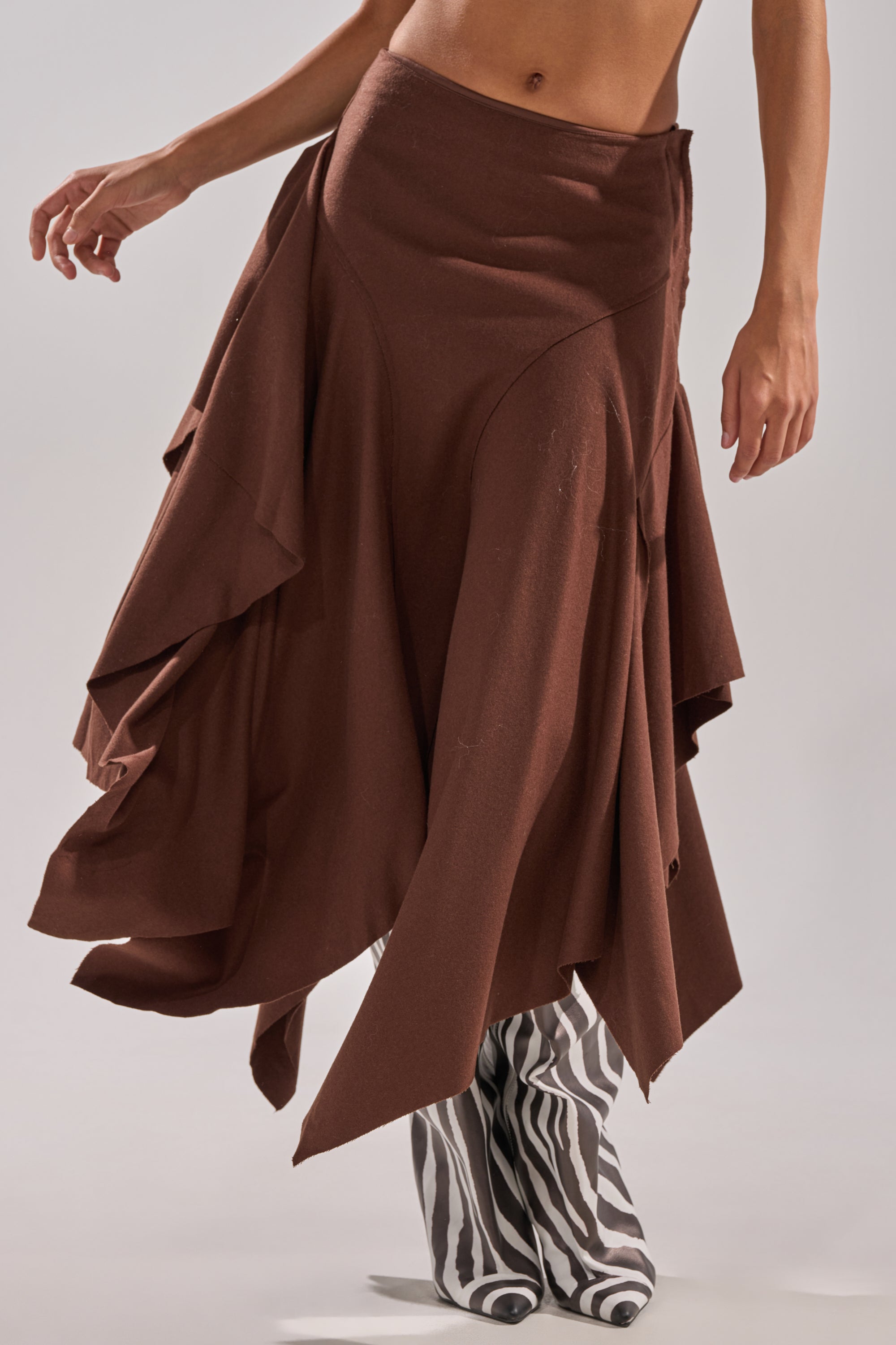A person modeling the FEELS GOOD MIDI SKIRT in brown with zebra-print boots, one arm bent, shown from the waist down against a light background. 2