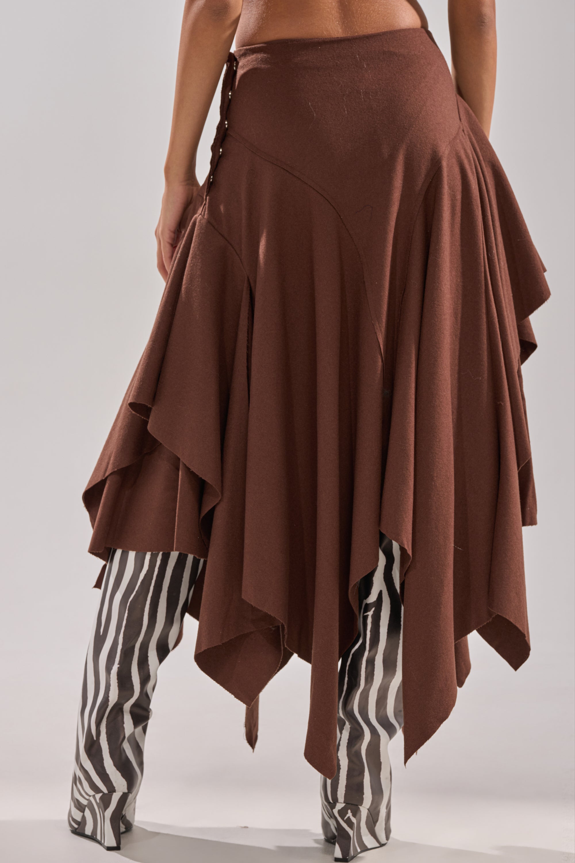 A person wearing the FEELS GOOD MIDI SKIRT with a pointed handkerchief hem, paired with black and white vertically striped boots. The image is cropped to show the body from waist to feet. 4