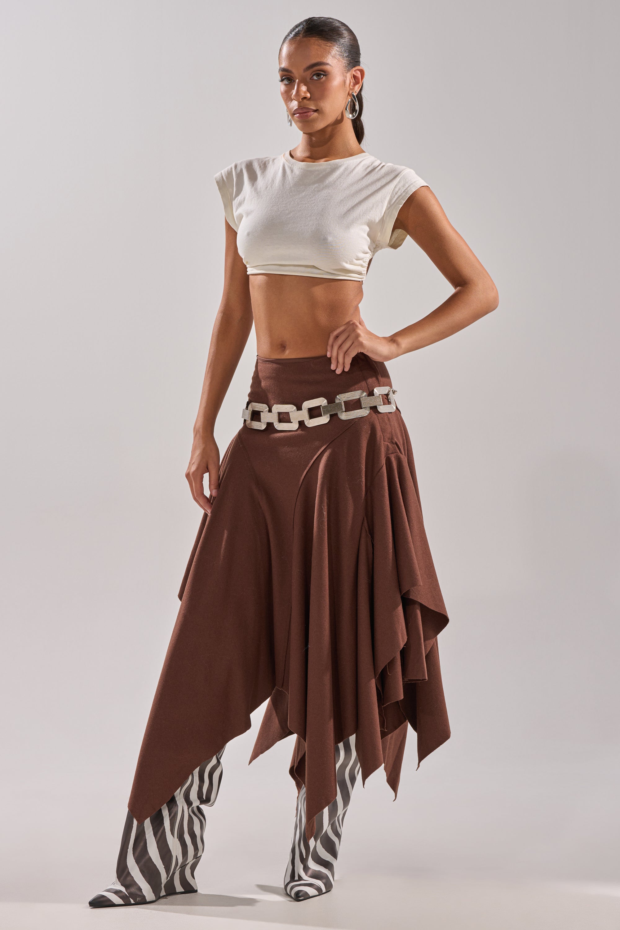 A woman poses in a white cropped top, the FEELS GOOD MIDI SKIRT with a chunky white belt, and zebra-print knee-high boots against a plain light background. 5