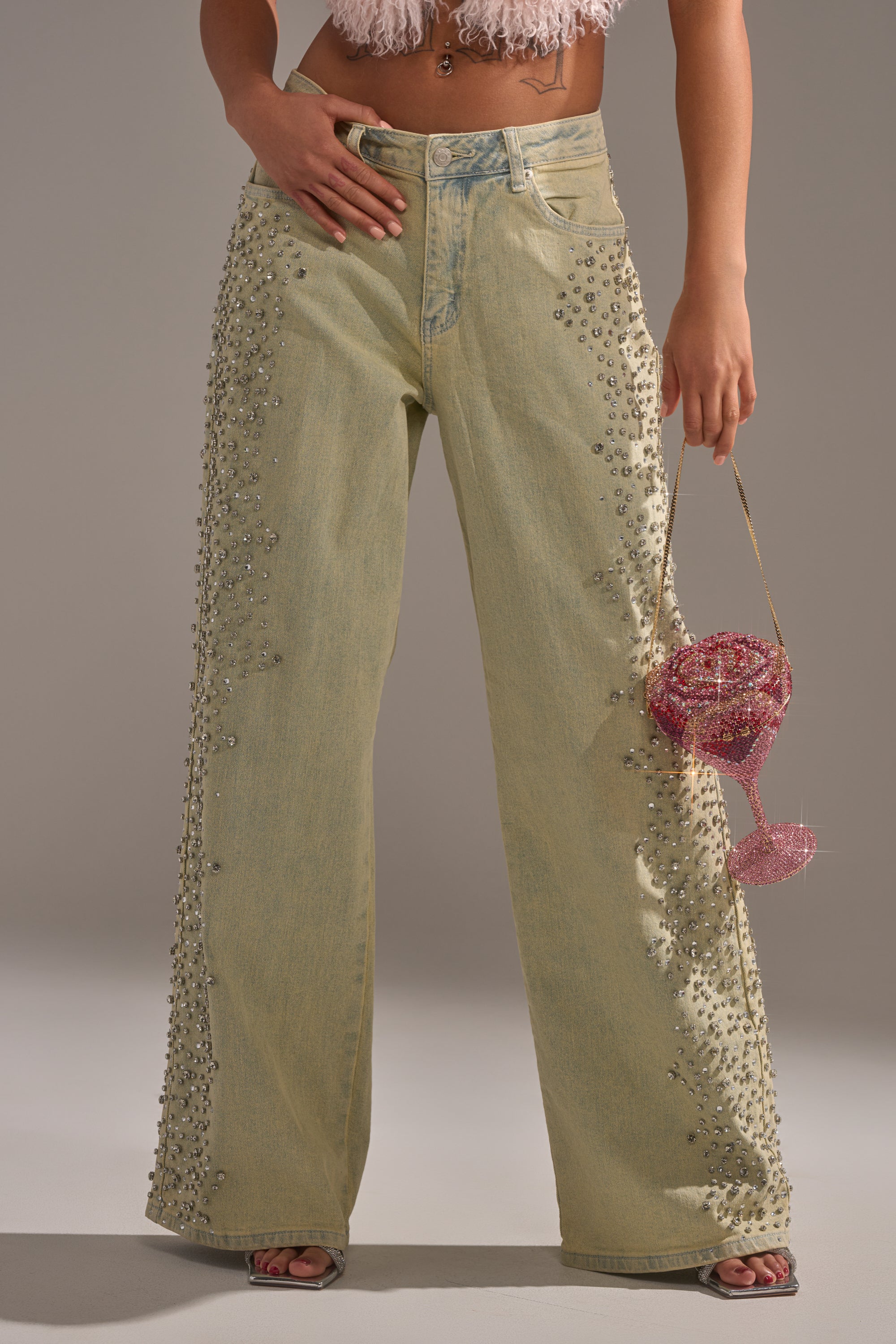 Wearing FEELING EXTREME RHINESTONE DENIM in light yellow with silver studs, a pink fuzzy crop top, and carrying a small beaded pink martini glass purse. 0