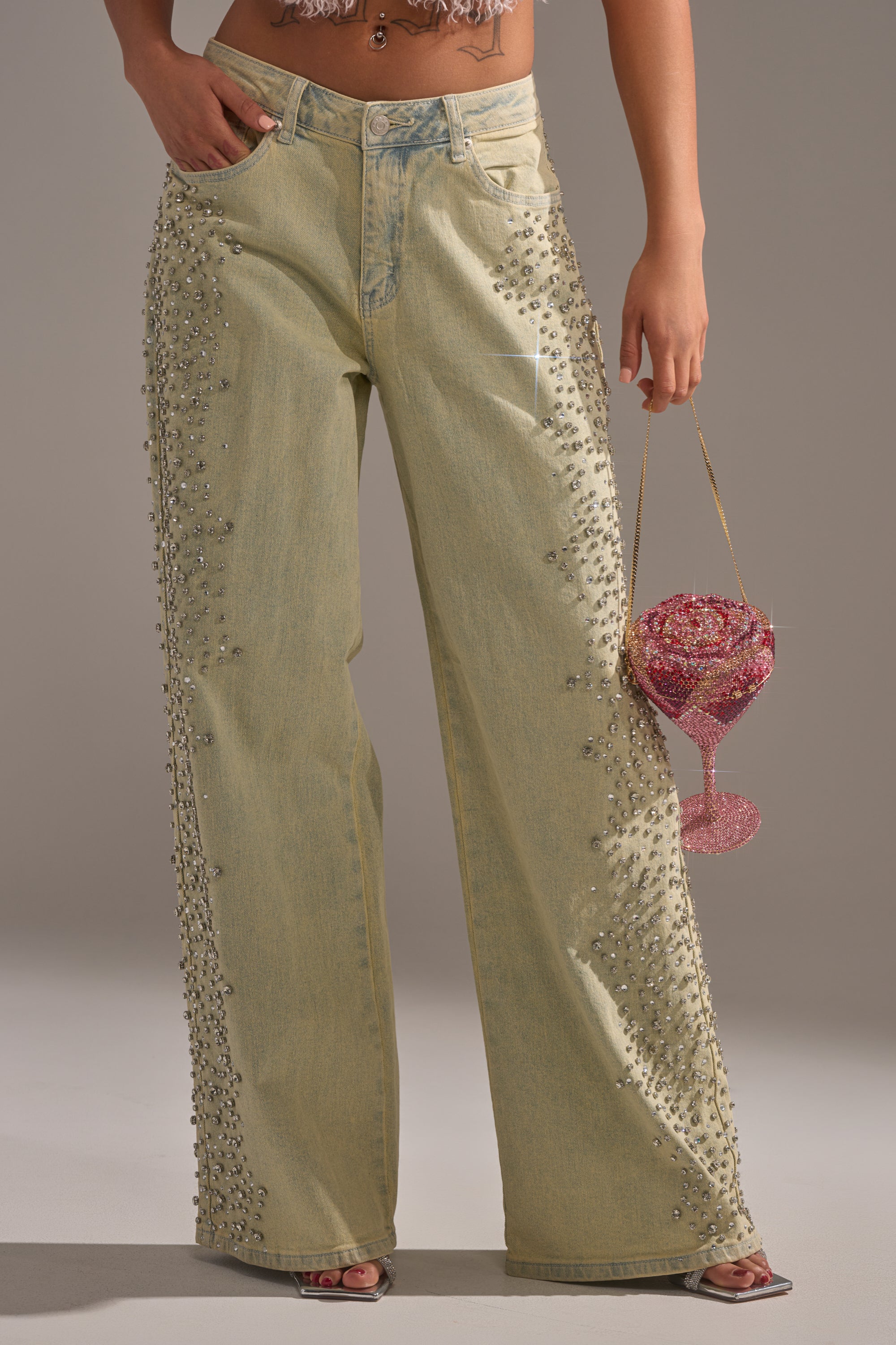 Wearing FEELING EXTREME RHINESTONE DENIM decorated with silver studs, a person (lower torso and legs visible) holds a sparkly pink beaded cocktail-glass-shaped handbag. 3