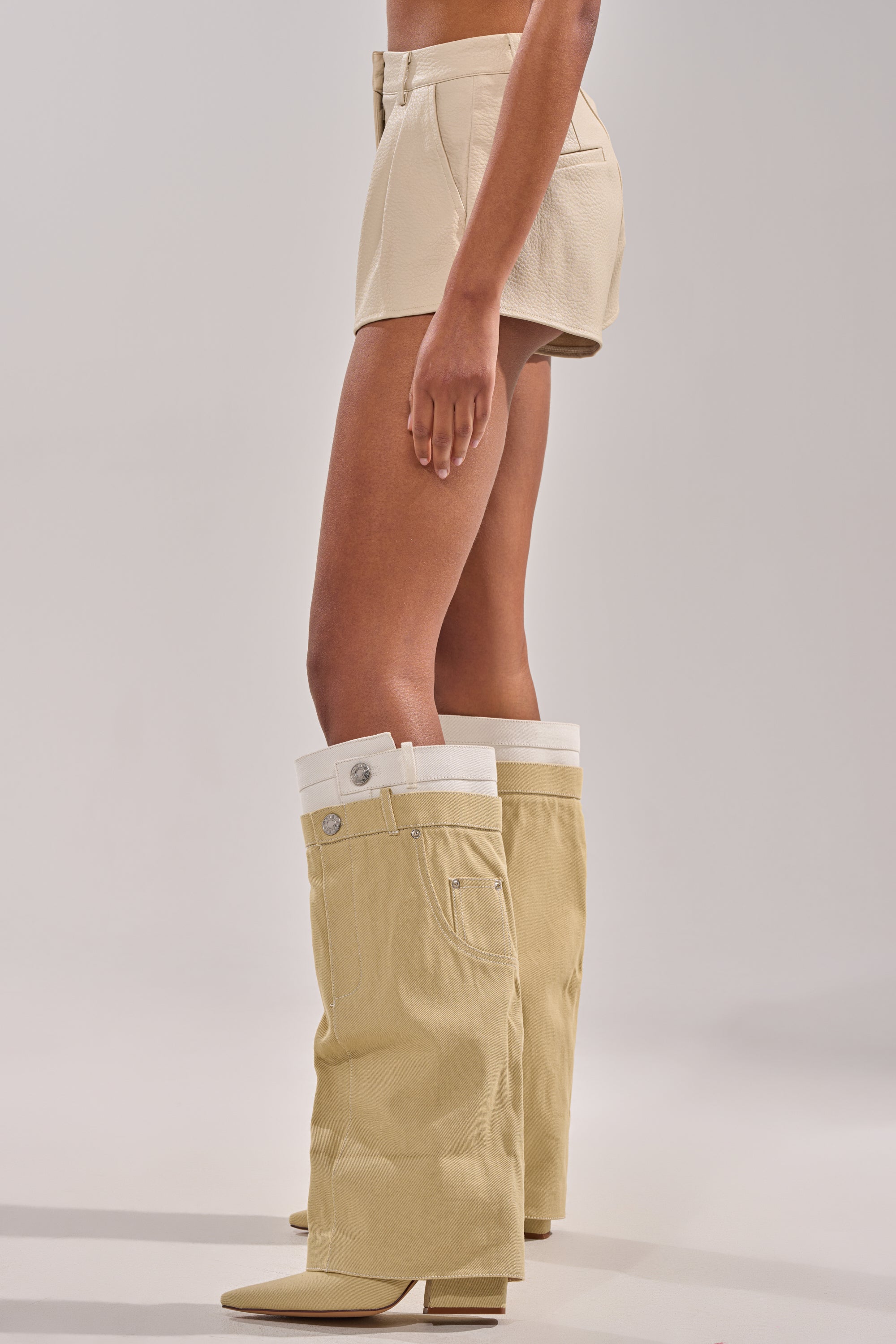 Someone wearing the UBAE LEATHER SHORT and distinctive tall beige boots resembling upside-down pants stands against a plain, light background. 3