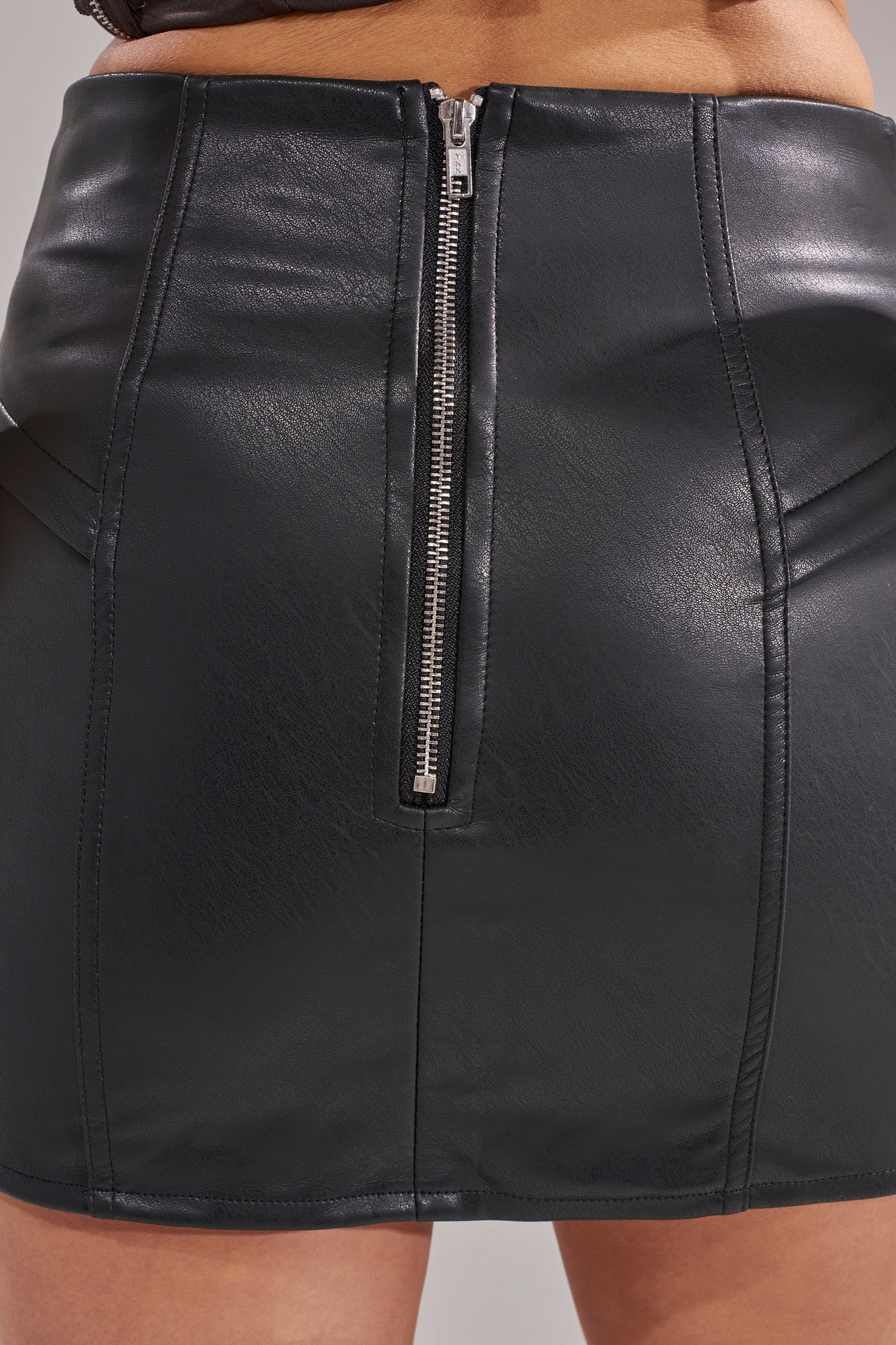 Close-up of the RIDE THAT WAVE FAUX LEATHER SKIRT, a curve-hugging, high-rise black mini with visible seams and a silver center zipper. 10