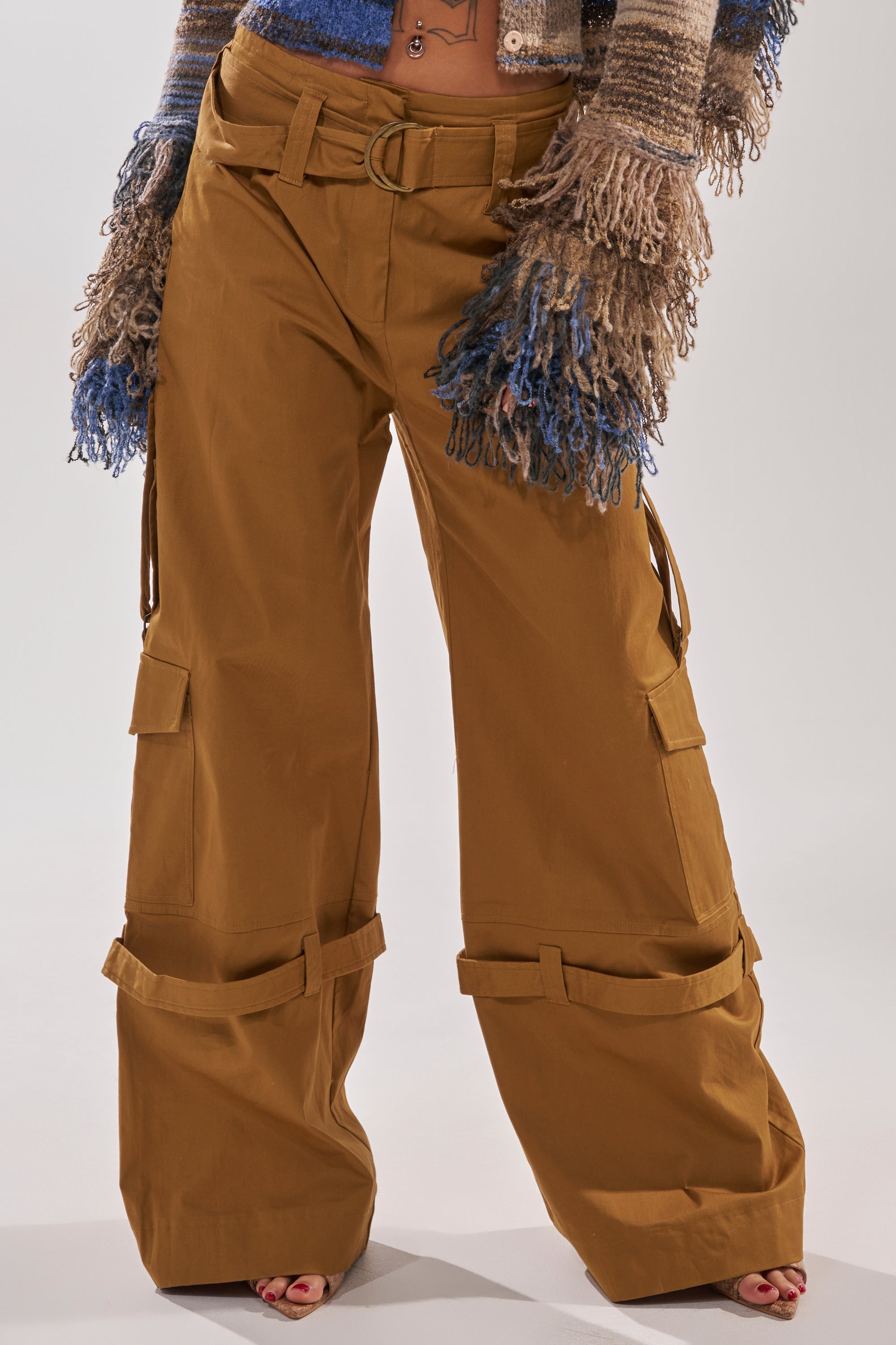 A person wears the DOWN FOR ANYTHING TROUSER—wide-leg, high-rise cargo pants with multiple pockets and a belt—paired with a textured fringe long-sleeve knit sweater, brown open-toed shoes, and colorful multicolored gloves. 1