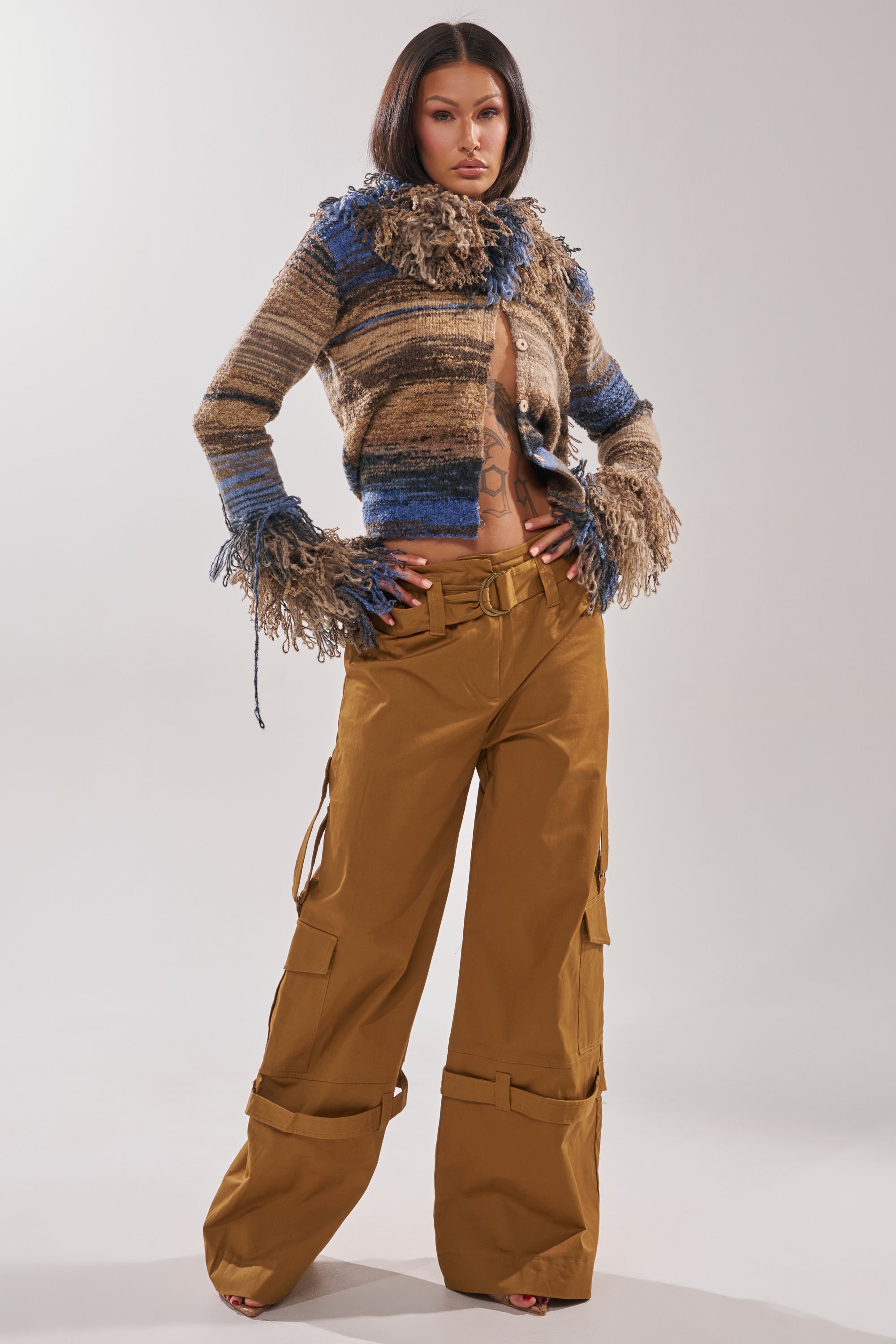 A woman stands confidently wearing the DOWN FOR ANYTHING TROUSER, a wide-leg cargo pant in brown, paired with a fuzzy, multi-colored cropped sweater with blue and brown tones and textured fringe on the sleeves and collar. 4