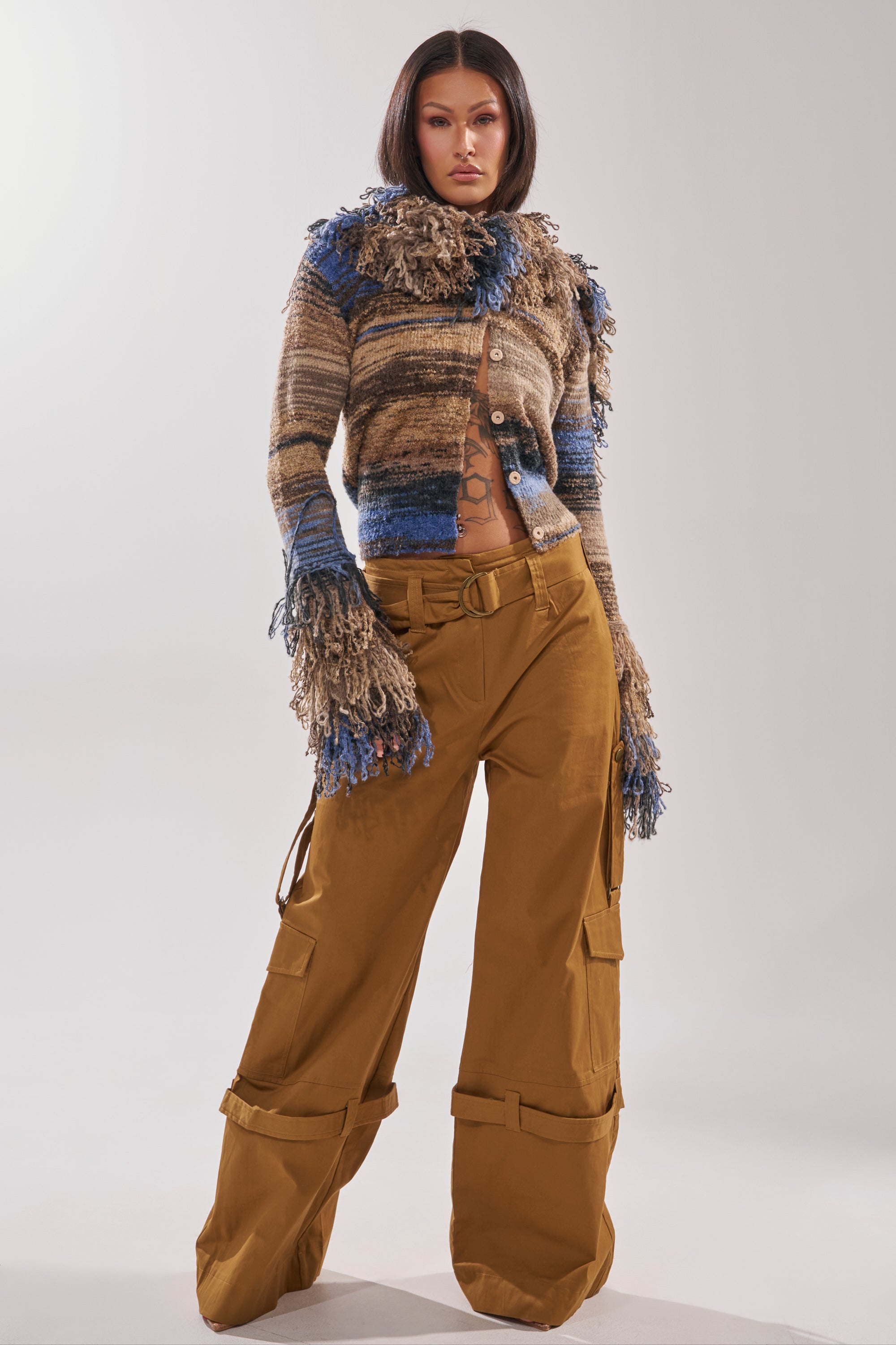A person with straight dark hair wears a textured, multicolored sweater with fringe and the DOWN FOR ANYTHING TROUSER, standing confidently against a plain, light background. 5
