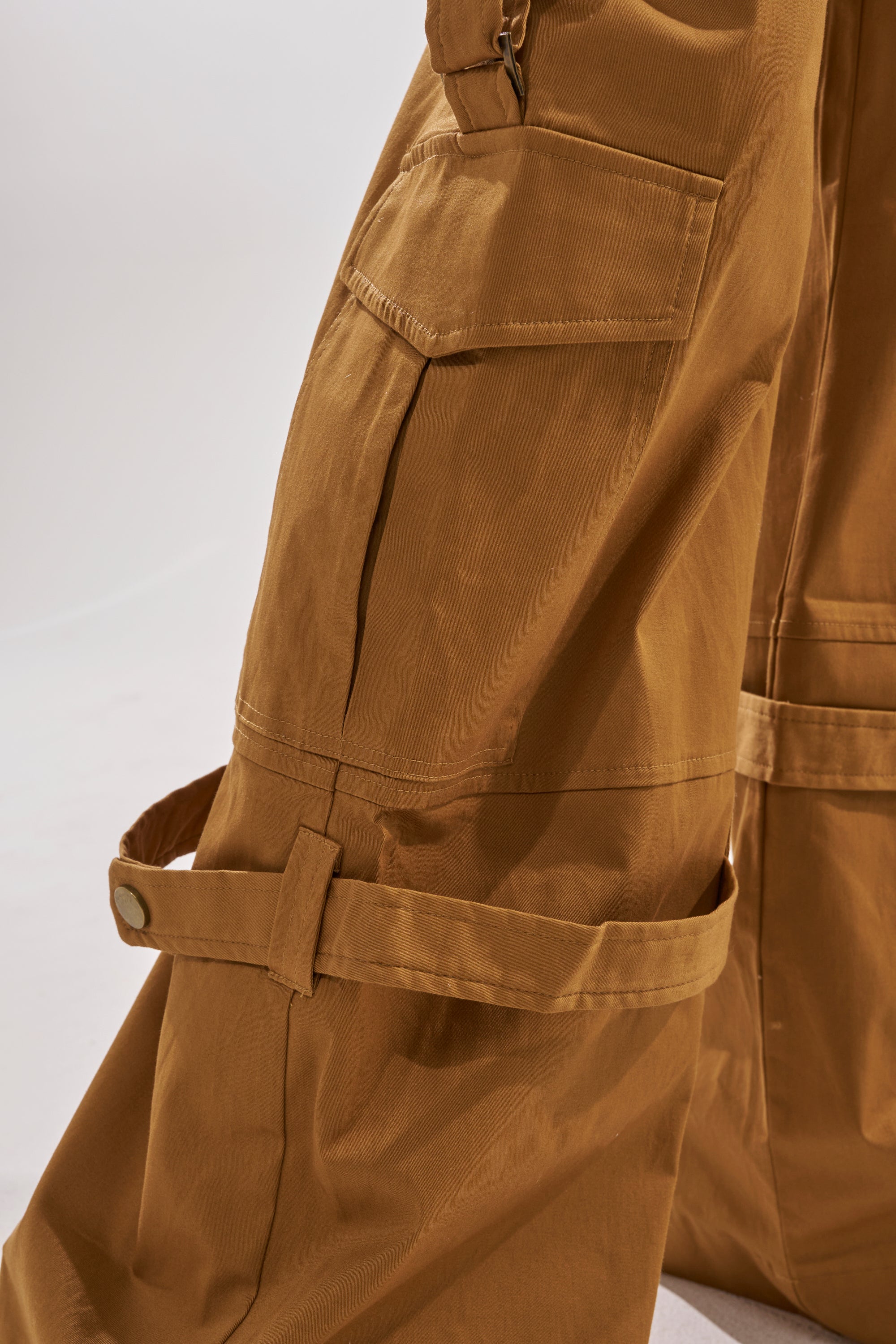 Close-up of the DOWN FOR ANYTHING TROUSER, showcasing its brown wide-leg cargo style with large side pockets, adjustable snap-button straps, and detailed fabric texture for a utilitarian look. 7