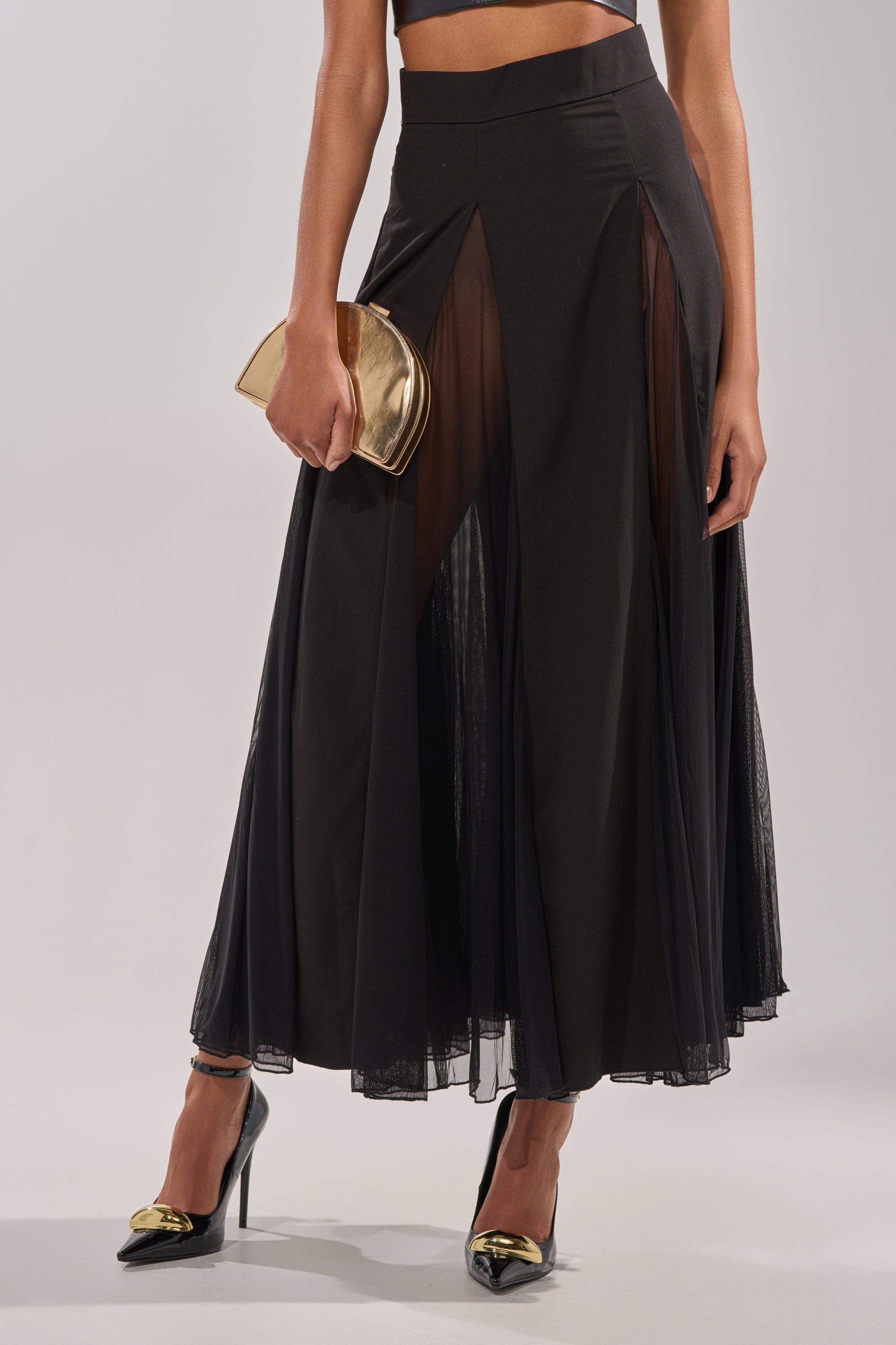 A woman wearing the SEXY MESH SKIRT, a matching crop top, black high heels with gold tips, and holding a small gold clutch. 0