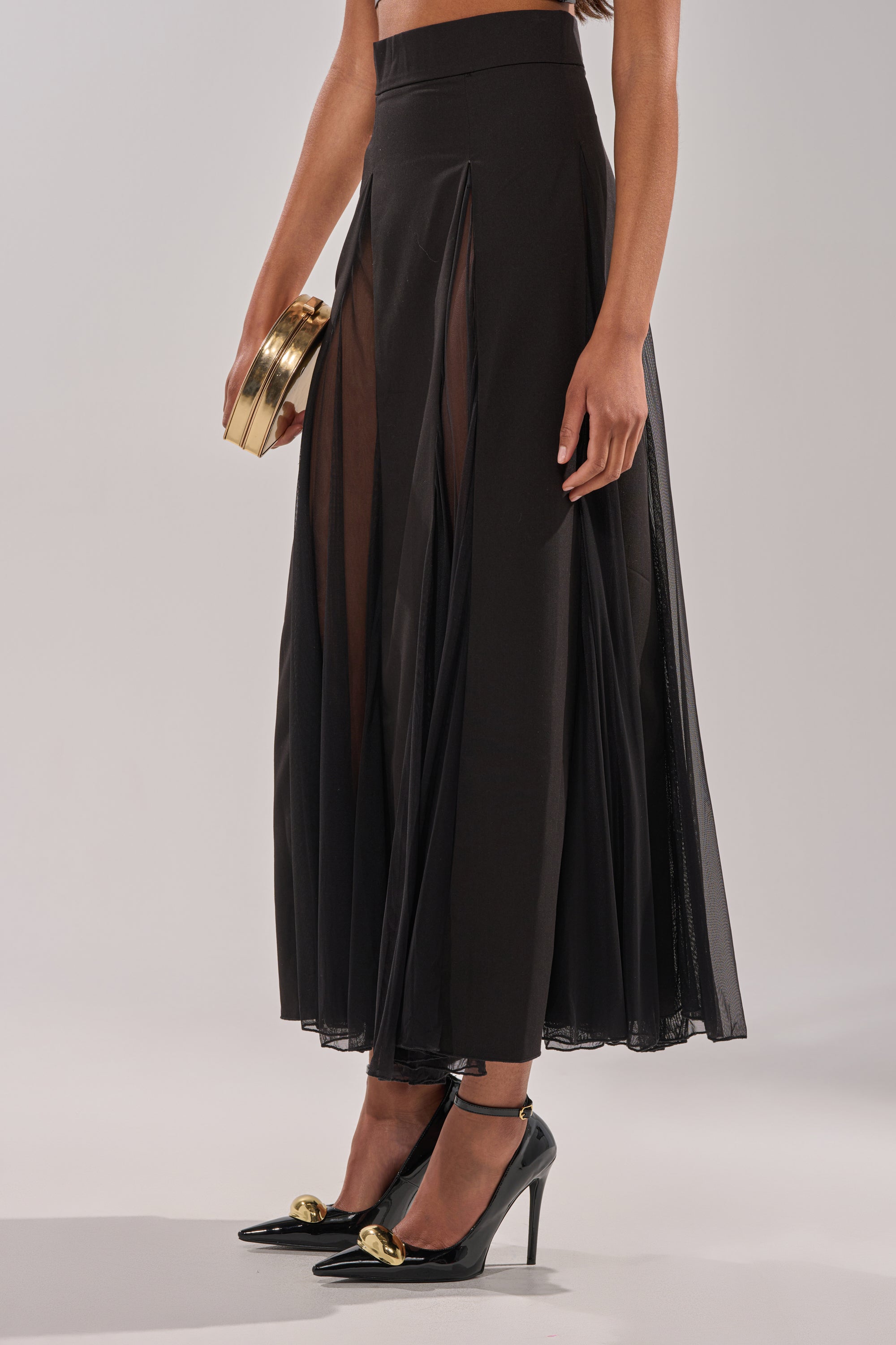 A woman wearing the SEXY MESH SKIRT with sheer panels, black high heels featuring gold details, and holding a small gold clutch. Her top half is cropped out of the image. 2