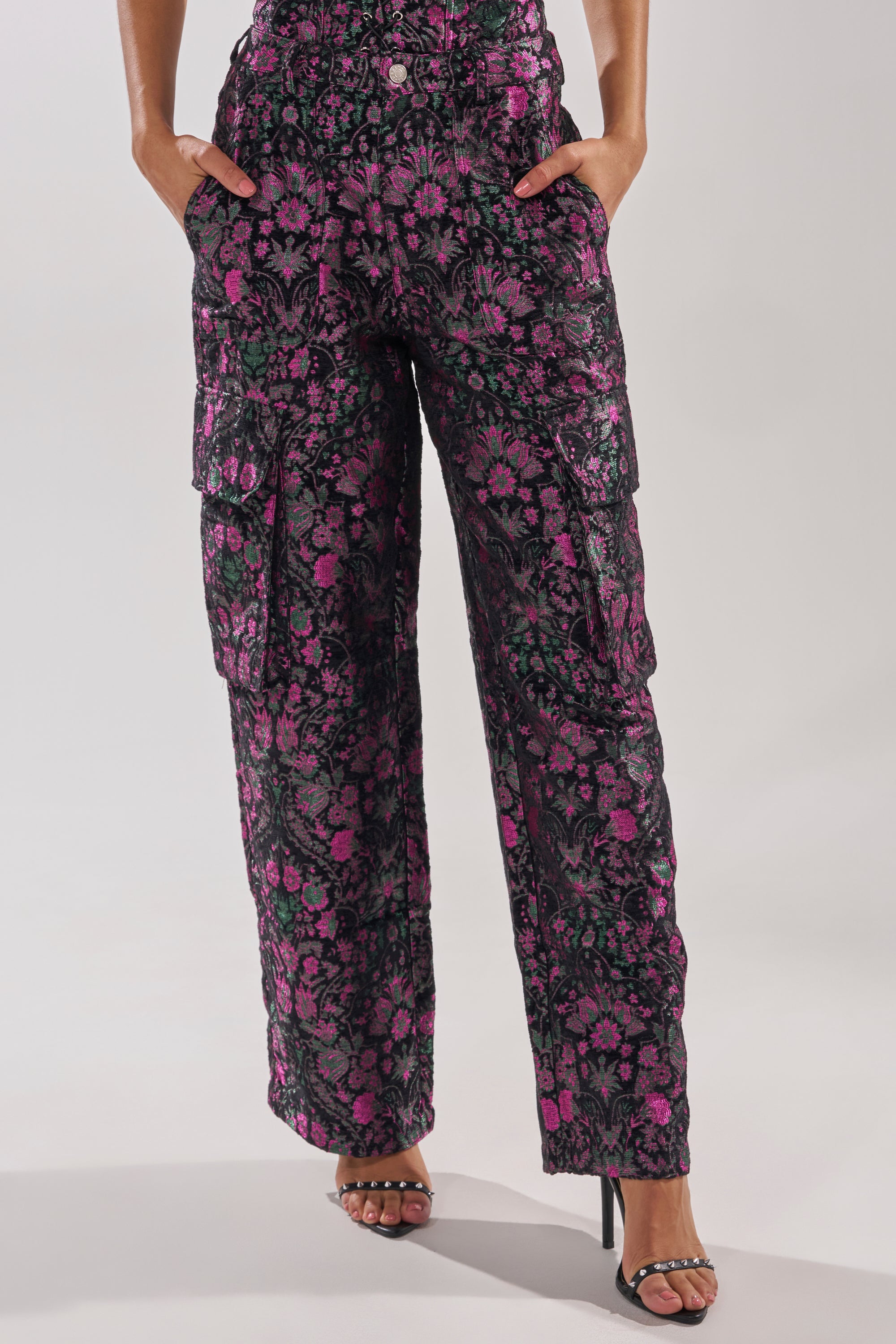 A person wears the KIMMY FLORAL TROUSER—high-rise cargo pants with pink and purple metallic floral details—paired with black high-heeled sandals. The photo is cropped at the torso. 2