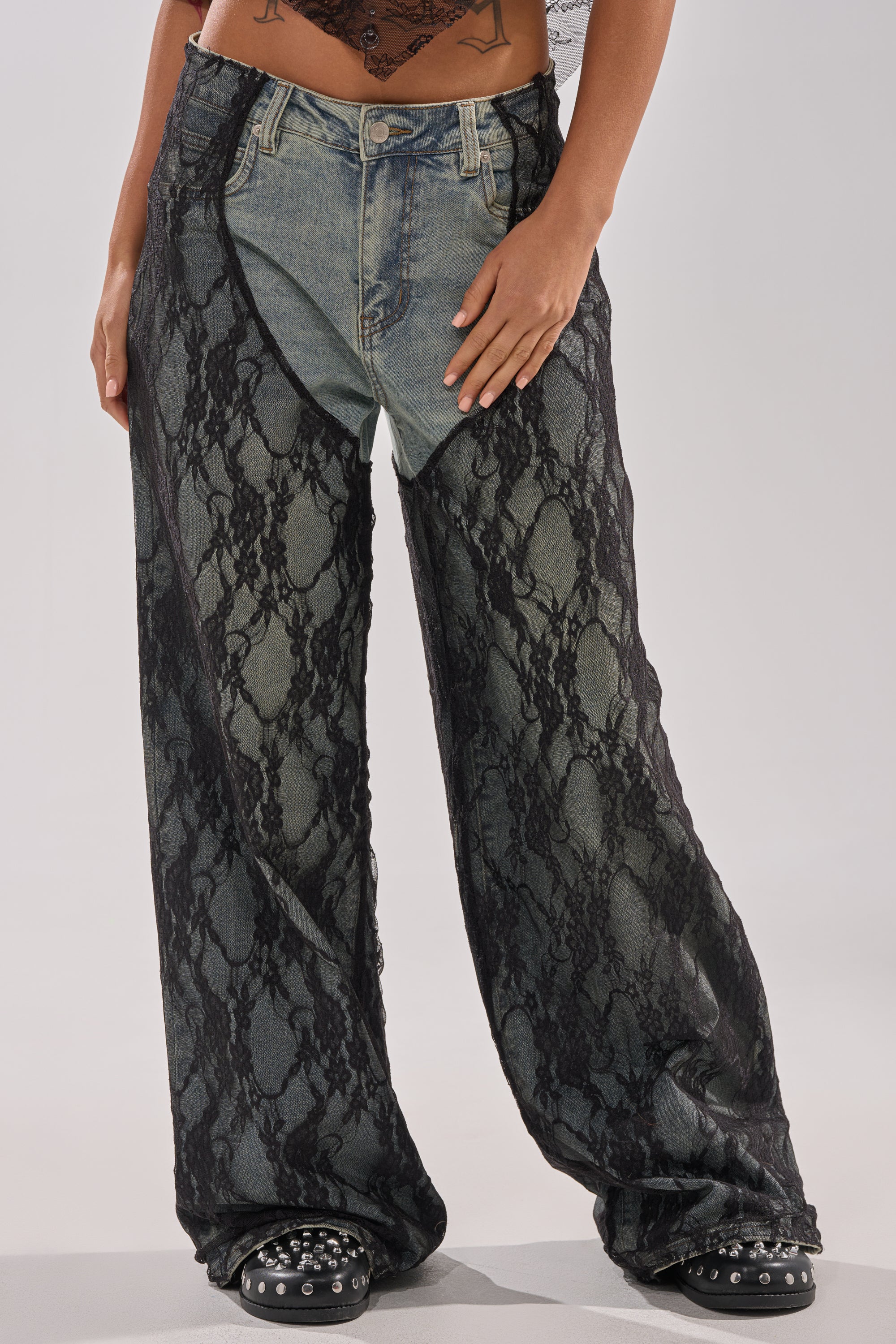 The model wears SEXY LACE CHAP DENIM—wide-leg jeans with a sheer black lace overlay—paired with black studded sandals. Only the lower torso and legs are shown. 3