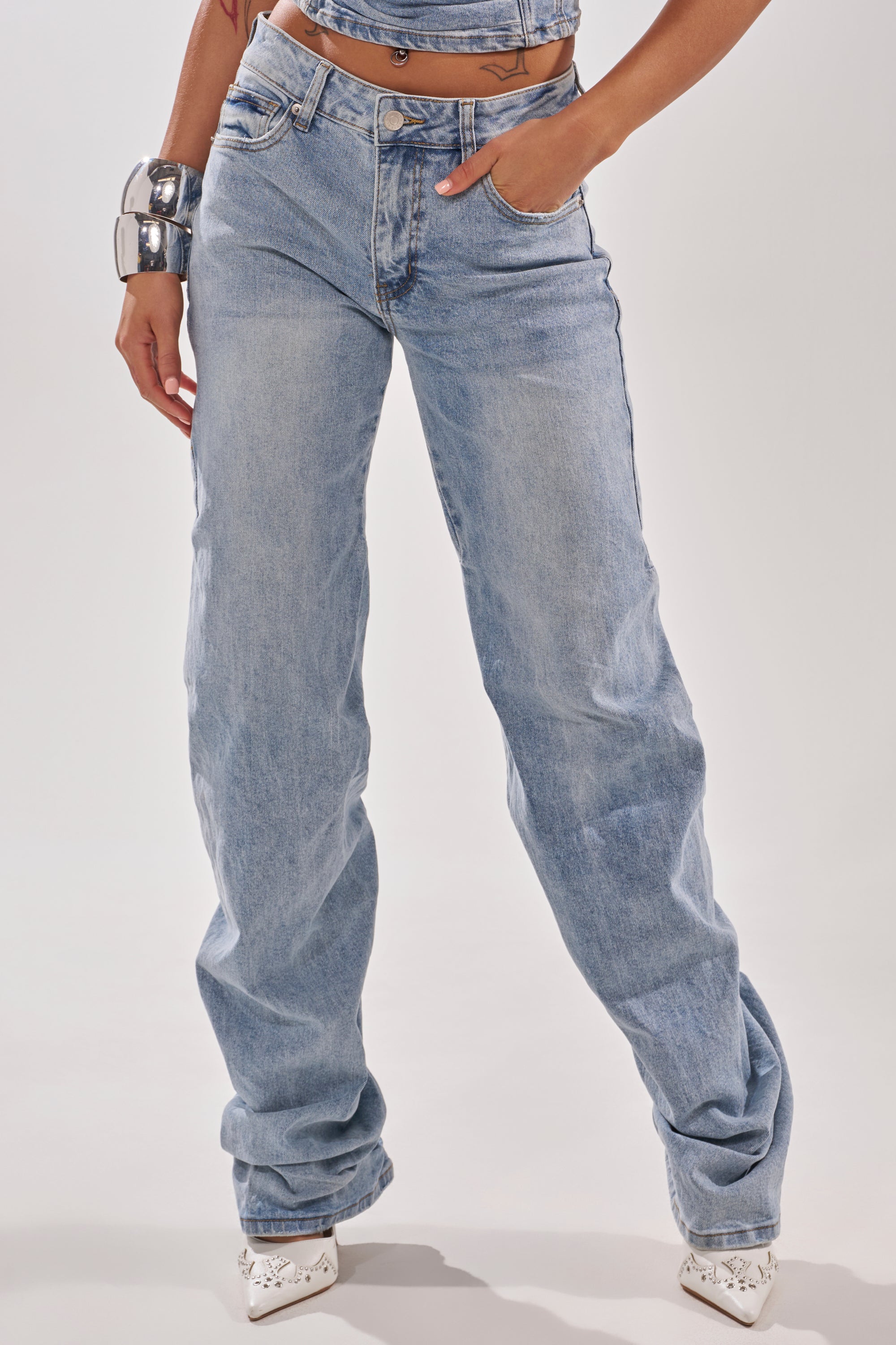 Wearing ON YOUR MIND STACKED DENIM jeans, a cropped top, white pointed shoes, and a chunky silver bracelet, a person poses with one hand in their pocket against a plain light background. 4