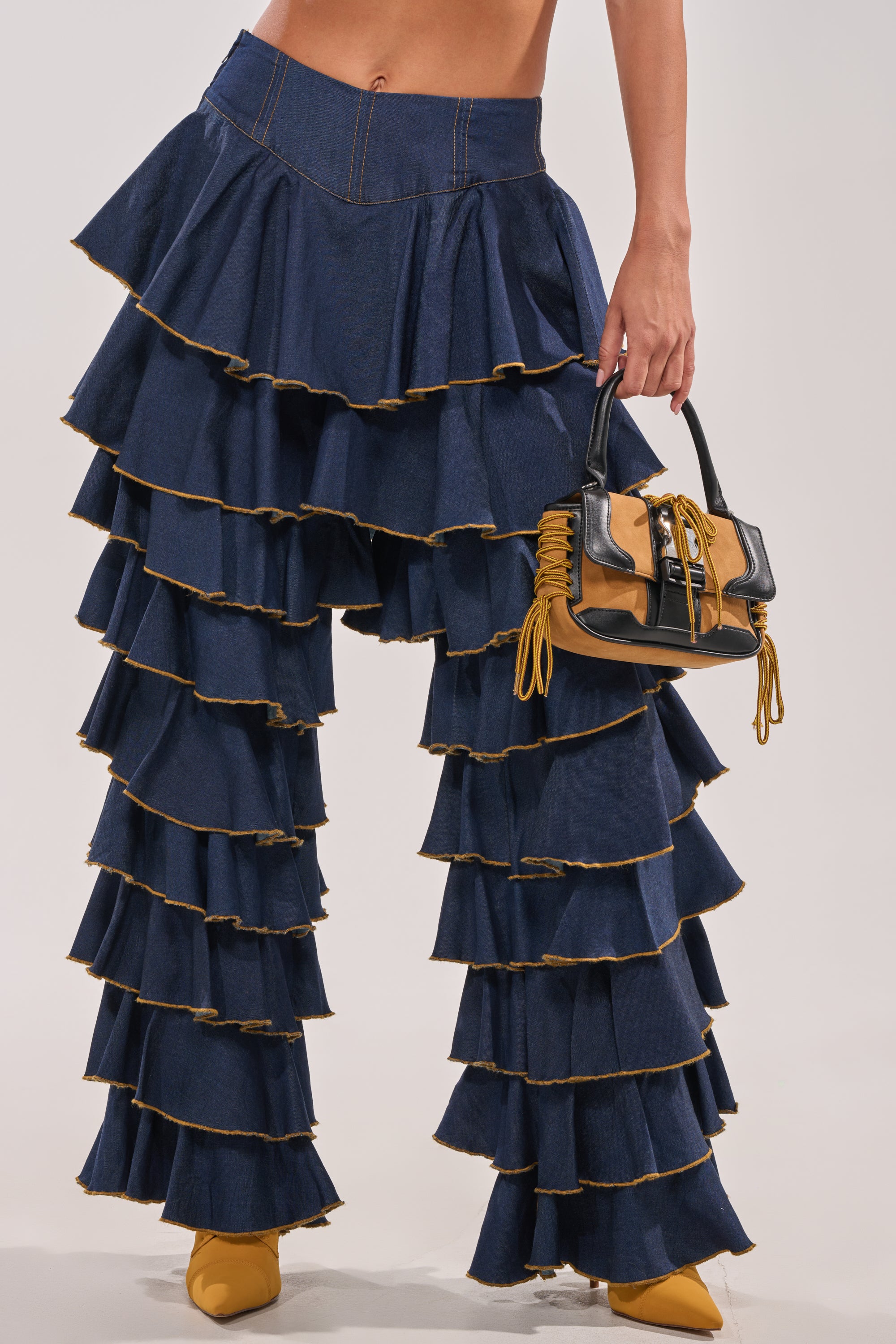 Wearing the SHAKE IT OUT DENIM RUFFLE JEANS with raw edges, yellow pointed-toe heels, and a brown-and-yellow handbag makes these statement jeans the standout piece of the look. 3