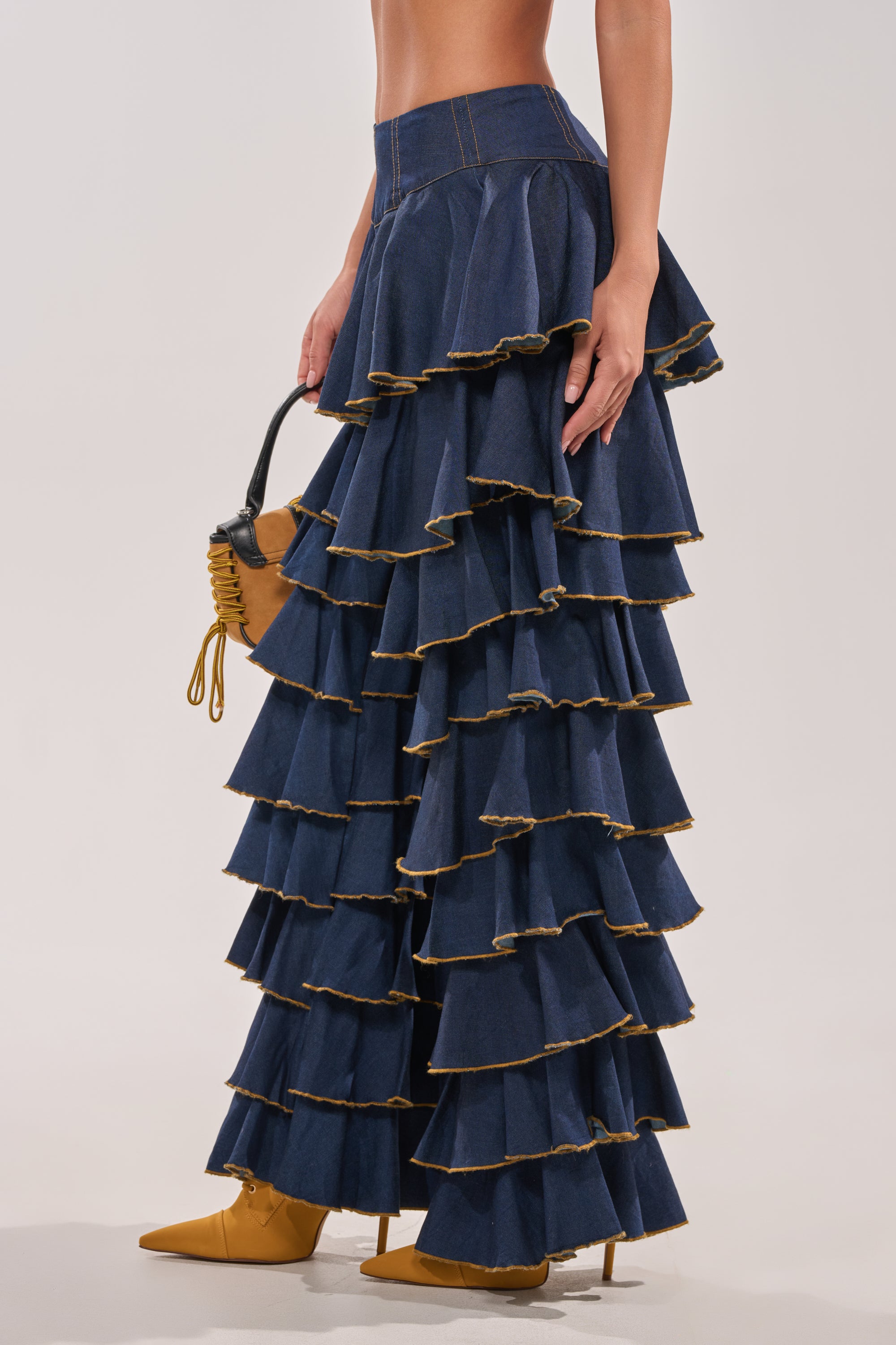 Wearing SHAKE IT OUT DENIM RUFFLE JEANS with gold trim, paired with a small brown handbag and mustard yellow pointed-toe shoes; only the lower half of the body is visible. 5