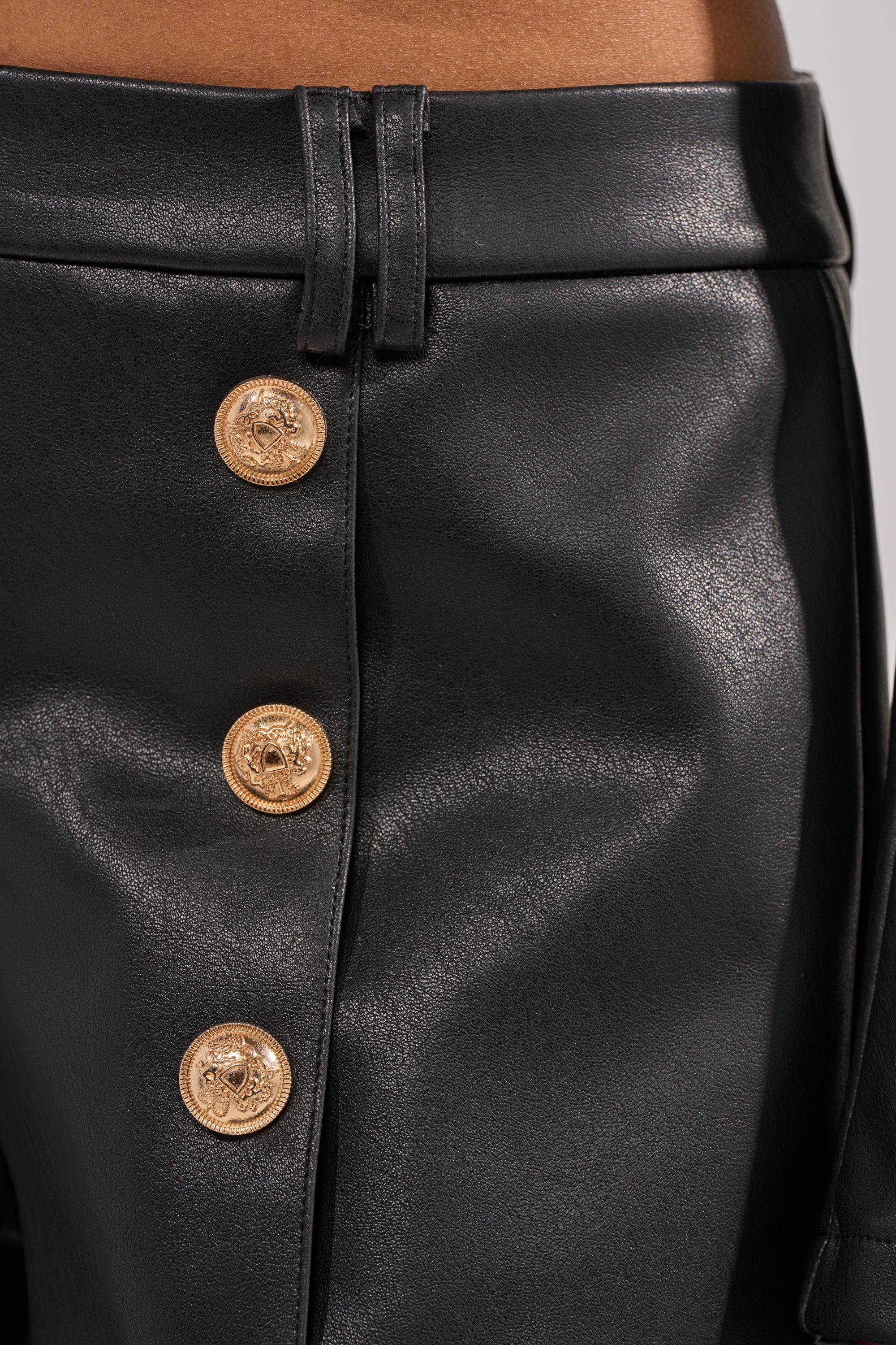 Close-up of LOLITA FAUX LEATHER SHORTS in black, detailed with shiny gold embossed buttons, belt loops, and visible stitching. 8
