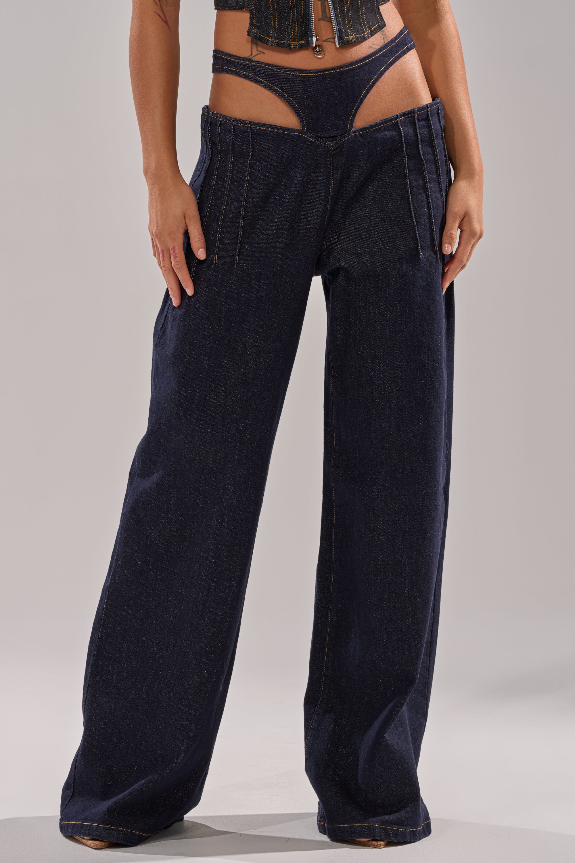A person wears the SEXY CAN I RELAXED DENIM, Y2K-inspired wide-leg jeans with a low-cut, strappy waistband and a cropped top, showcasing modern style and revealing the hips and waist. 0