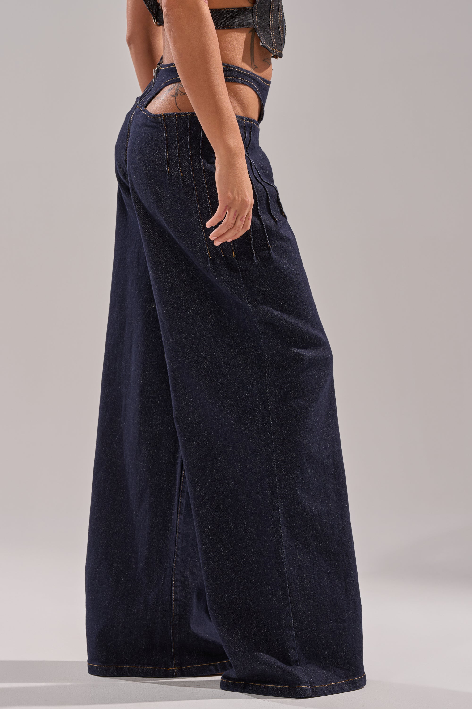 Wearing the SEXY CAN I RELAXED DENIM wide-leg pants with cut-out details at the waistband and sides, styled with a cropped top. Side photo highlights the unique design. 2
