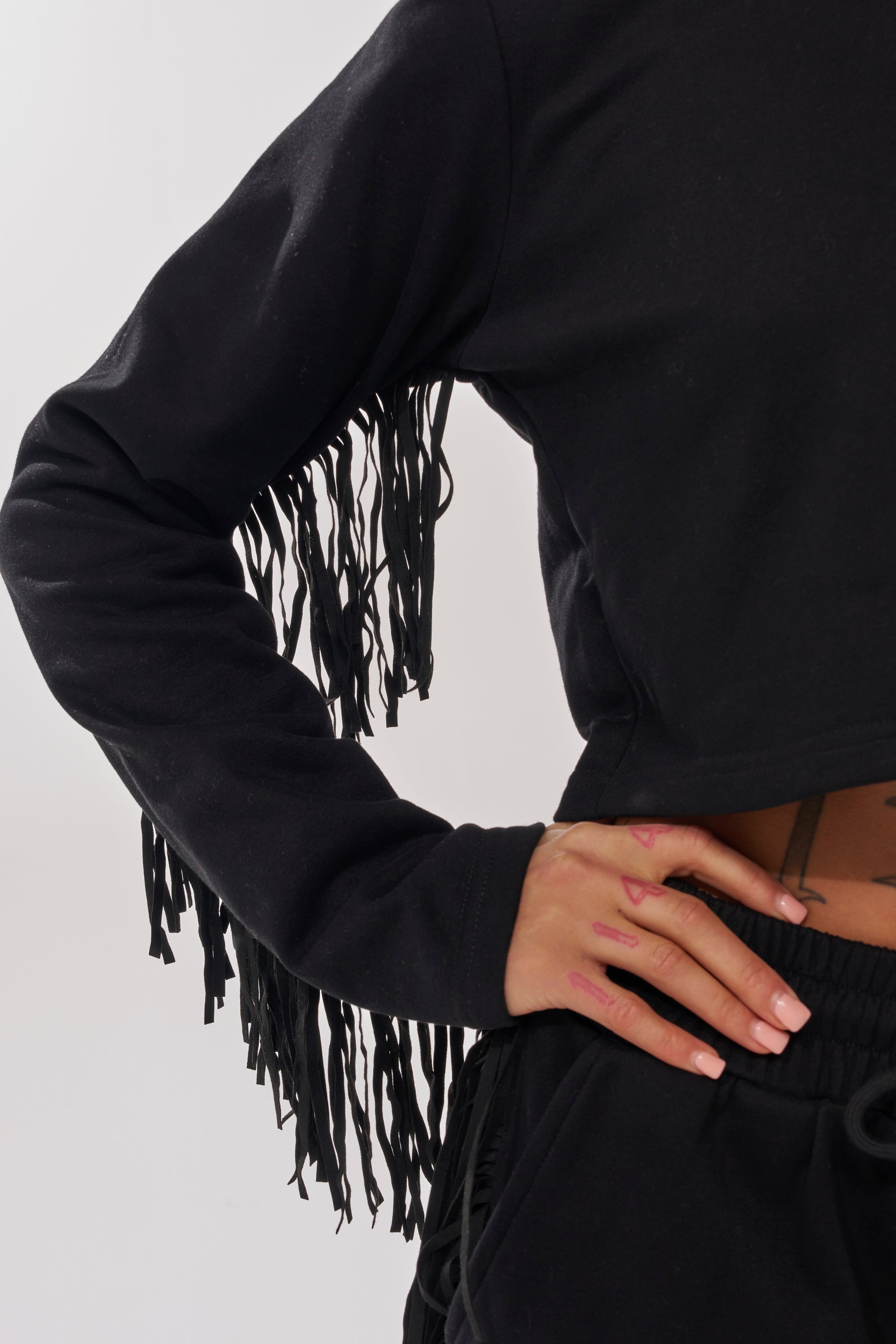A person wears the PLAYING CARDS CROP SWEATSHIRT with black pants, posing with one hand on their hip. Only the torso and one arm are visible. 9