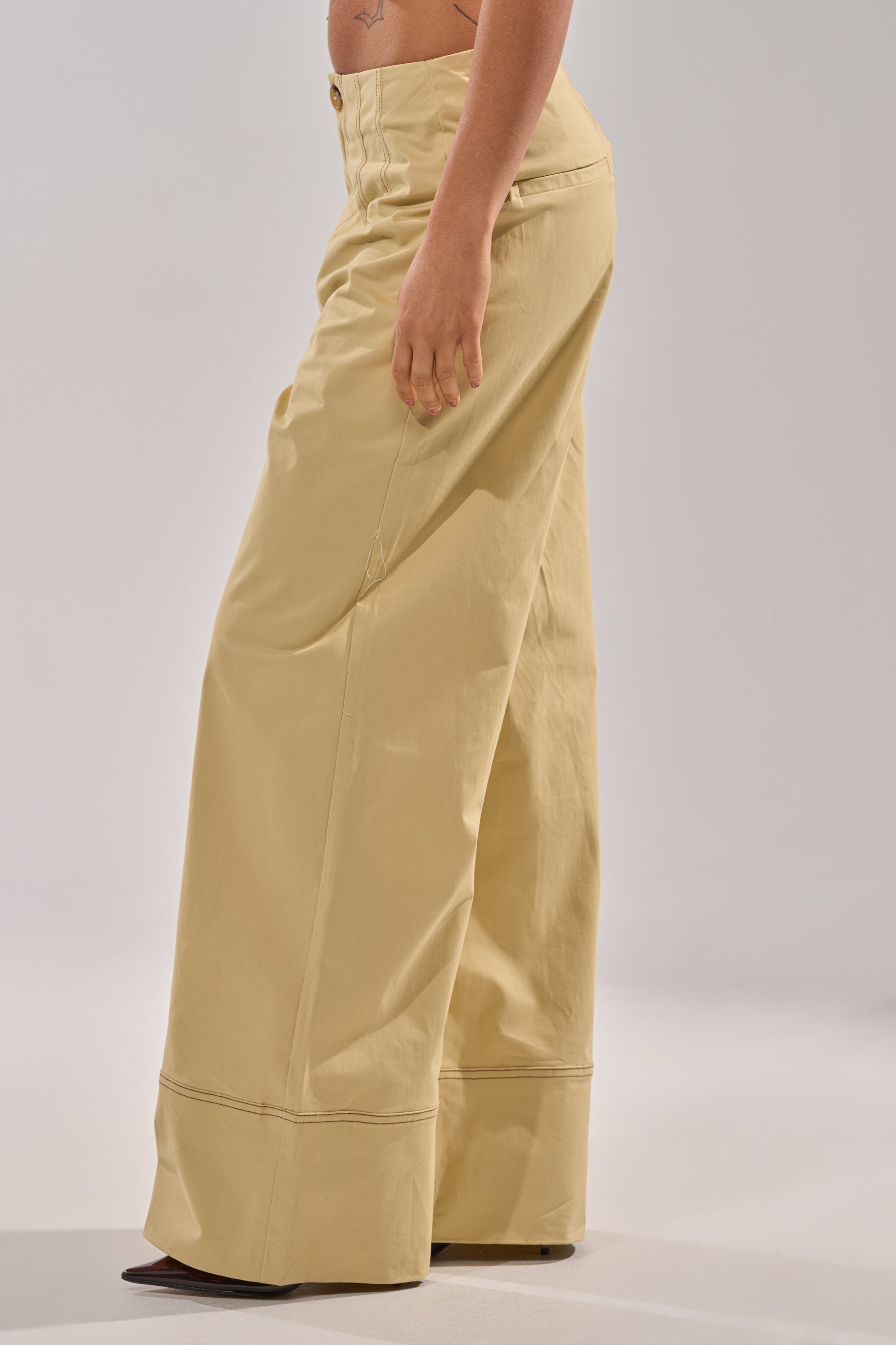 The lower torso and legs of a person, shown sideways against a plain background, wear DIANA WIDE LEG PANTS—business-casual khaki with a high-rise waist and visible seams—paired with dark pointed shoes. 2