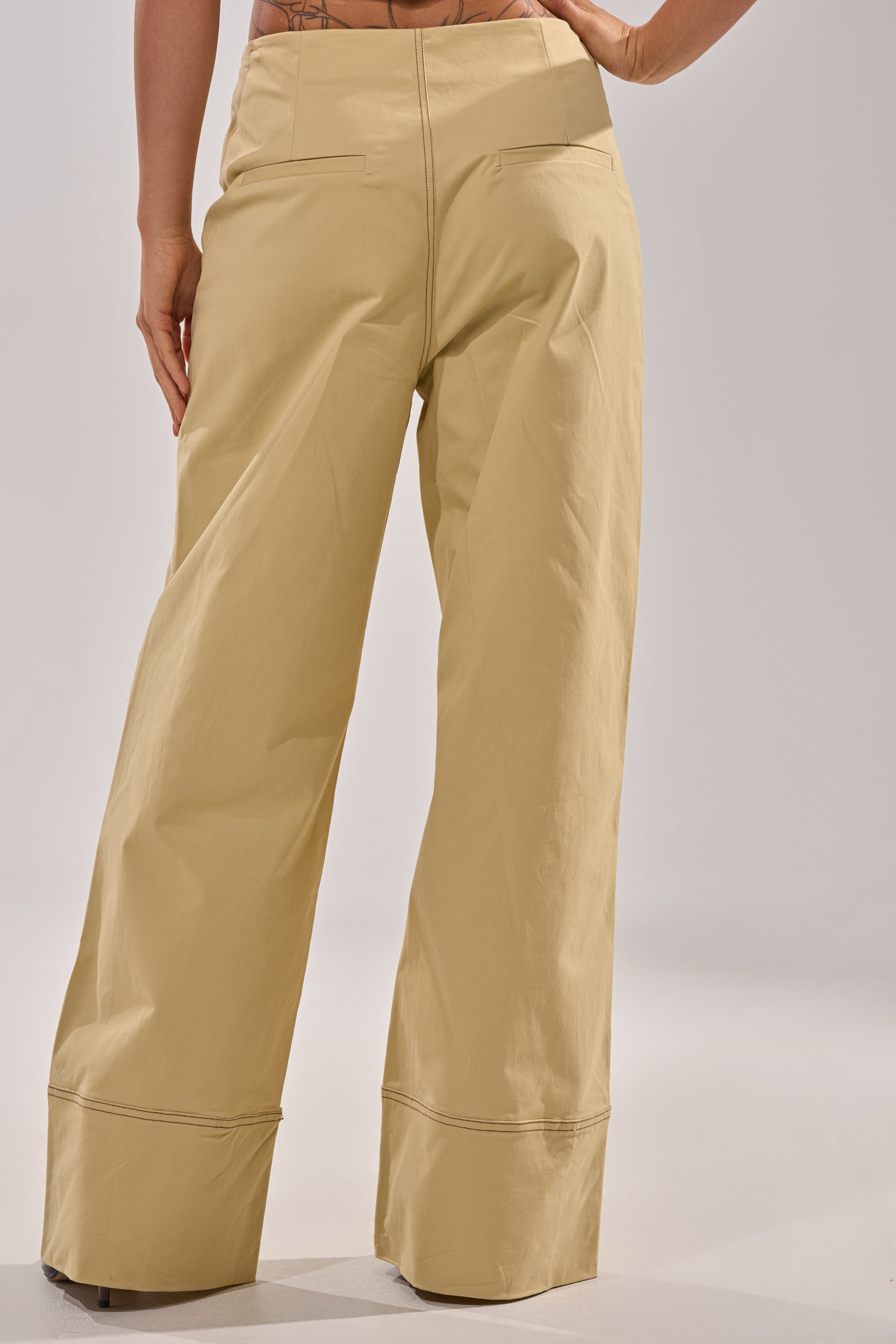 A person stands with their back to the camera against a plain background, wearing DIANA WIDE LEG PANTS in khaki with a high-rise waist, one hand resting on their hip. 3